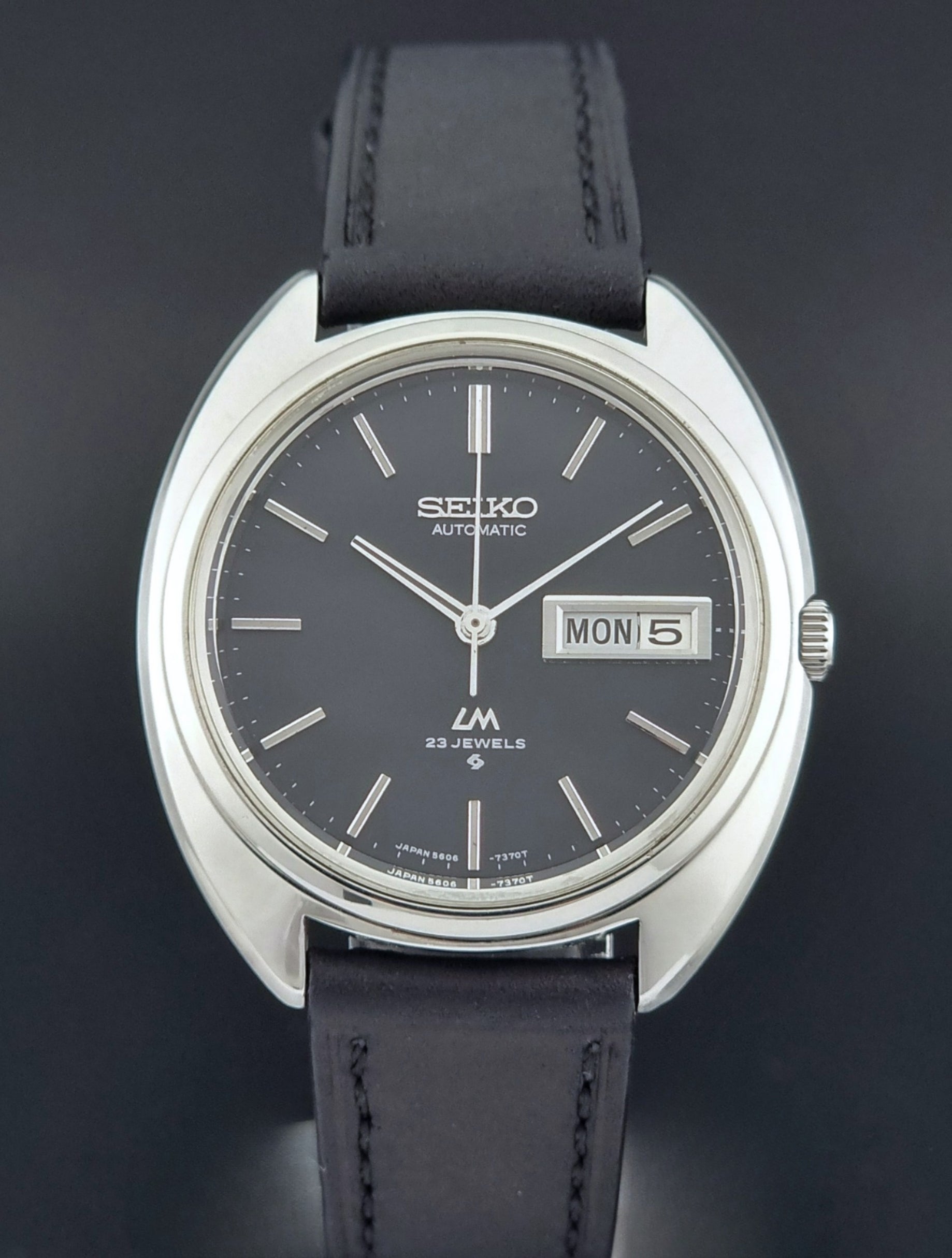 Vintage Seiko watch LordMatic 5606-7150 with black leather strap on a brown leather surface front view