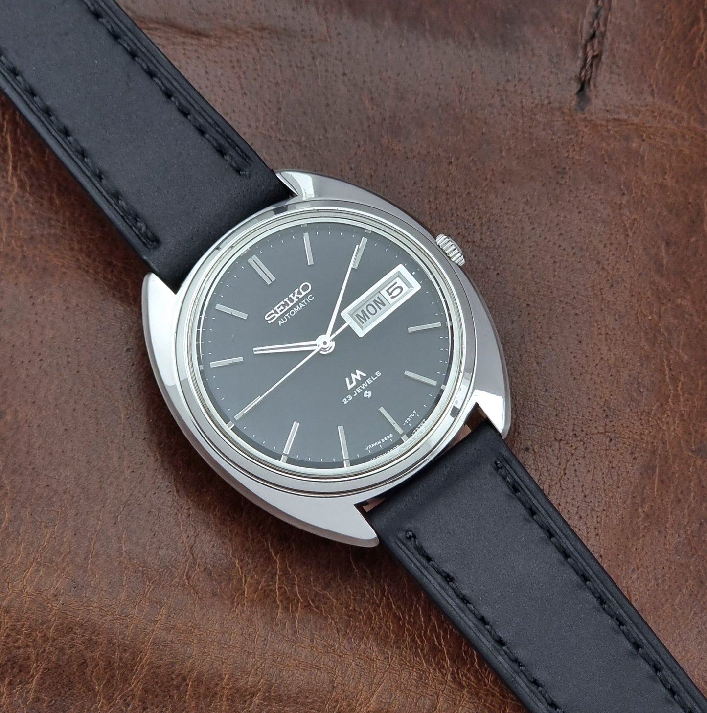 Vintage Seiko watch LordMatic 5606-7150 with black leather strap on a brown leather surface