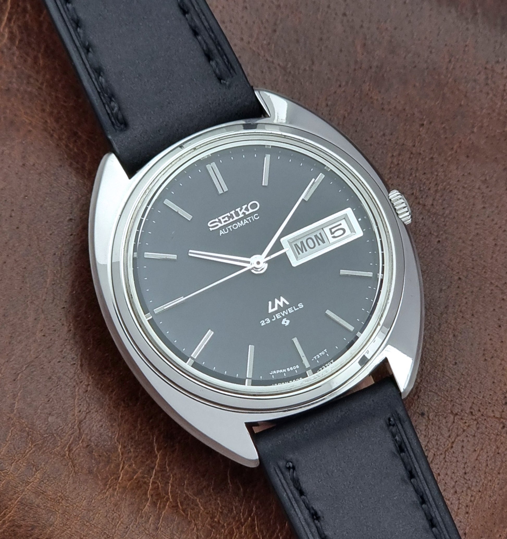 Vintage Seiko watch LordMatic 5606-7150 with black leather strap on a brown leather surface close up