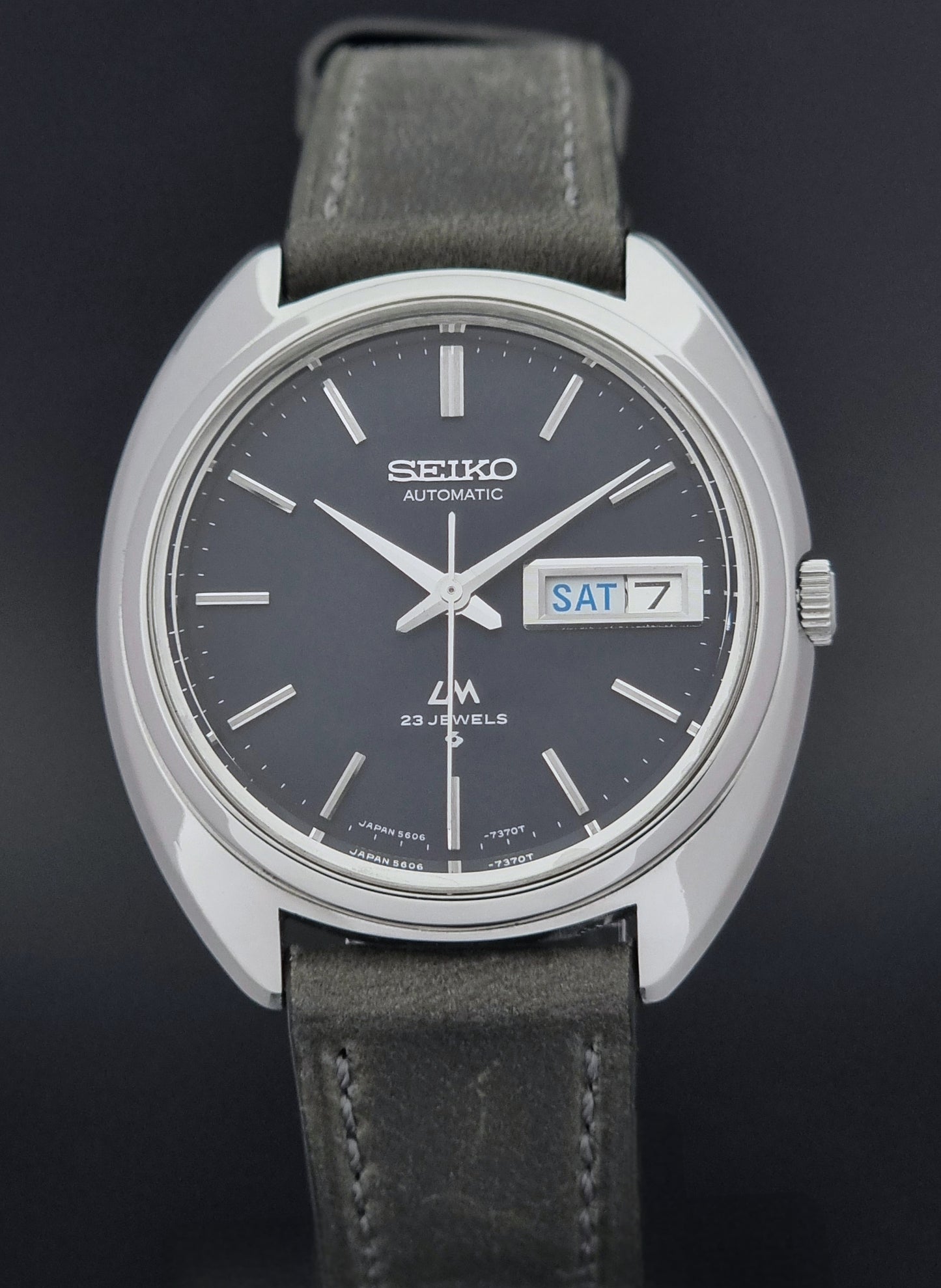 Vintage Seiko Lordmatic 5606-7150 wristwatch with a dark gray strap on a dark background close front view