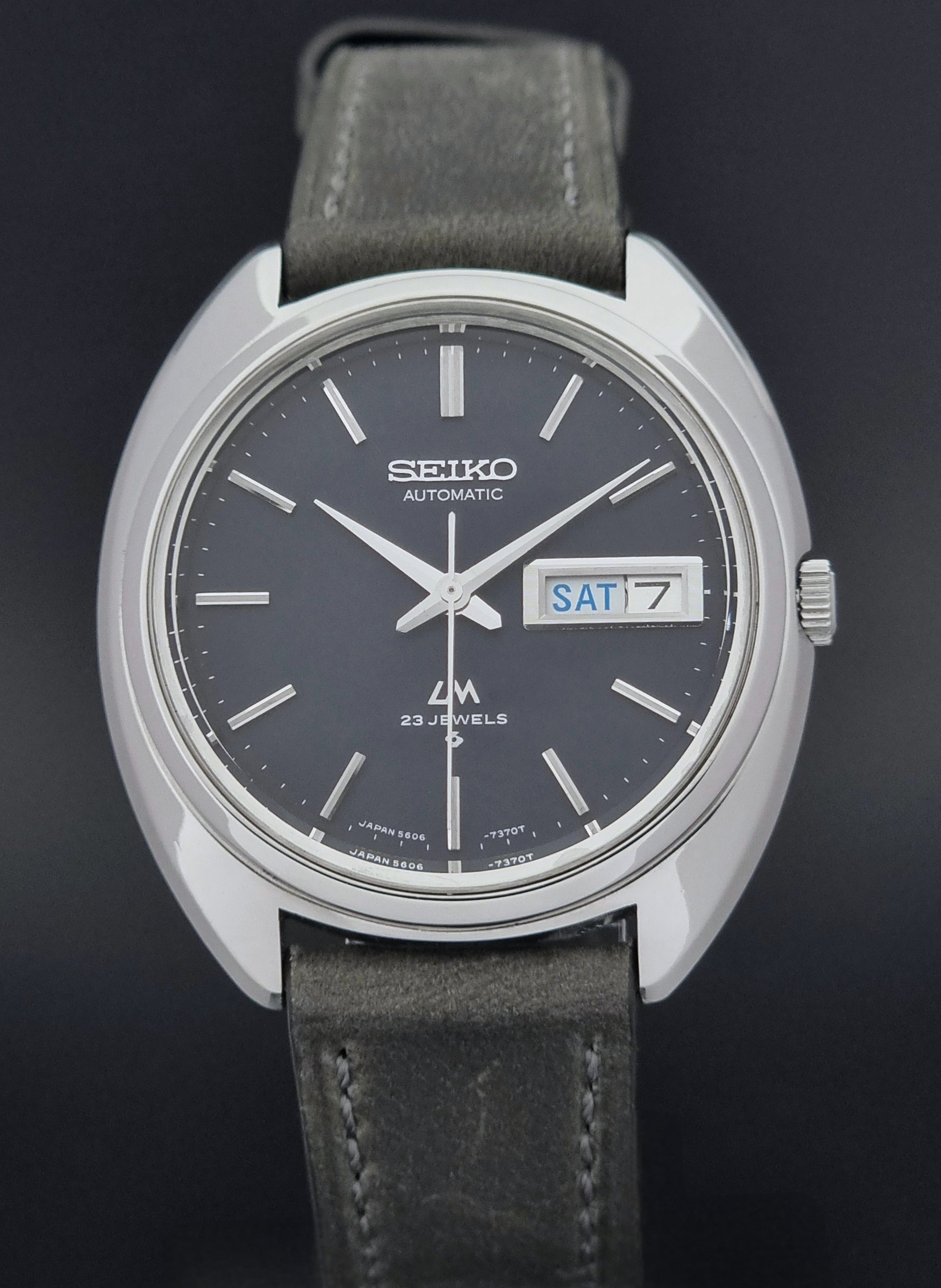 Vintage Seiko Lordmatic 5606-7150 wristwatch with a dark gray strap on a dark background close front view