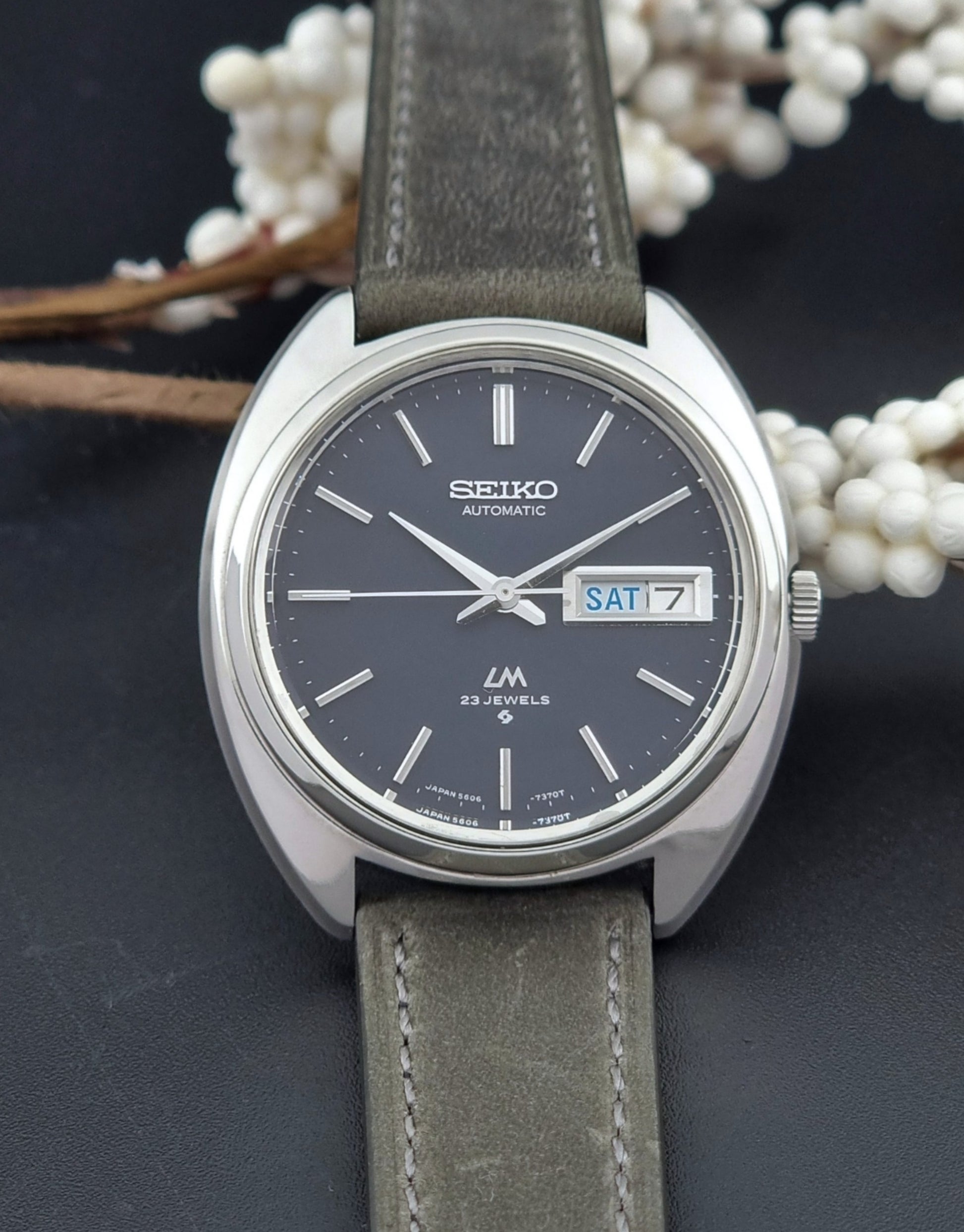 Vintage Seiko Lordmatic 5606-7150 wristwatch with a dark gray strap on a dark background front view