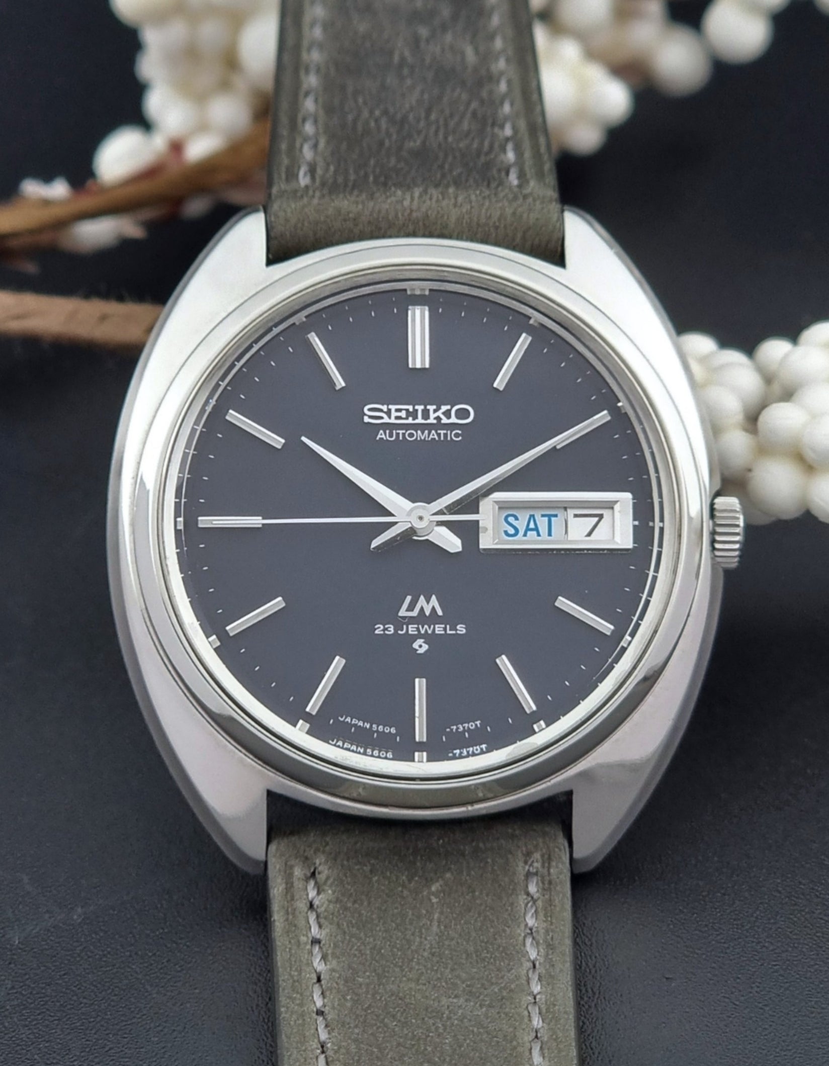 Vintage Seiko Lordmatic 5606-7150 wristwatch with a dark gray strap on a dark background dial view
