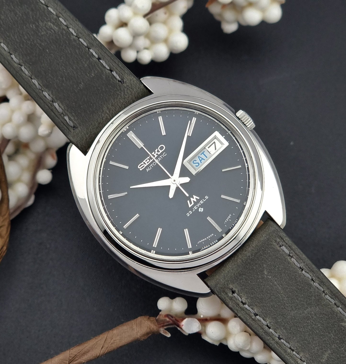 Vintage Seiko Lordmatic 5606-7150 wristwatch with a dark gray strap on a dark background front