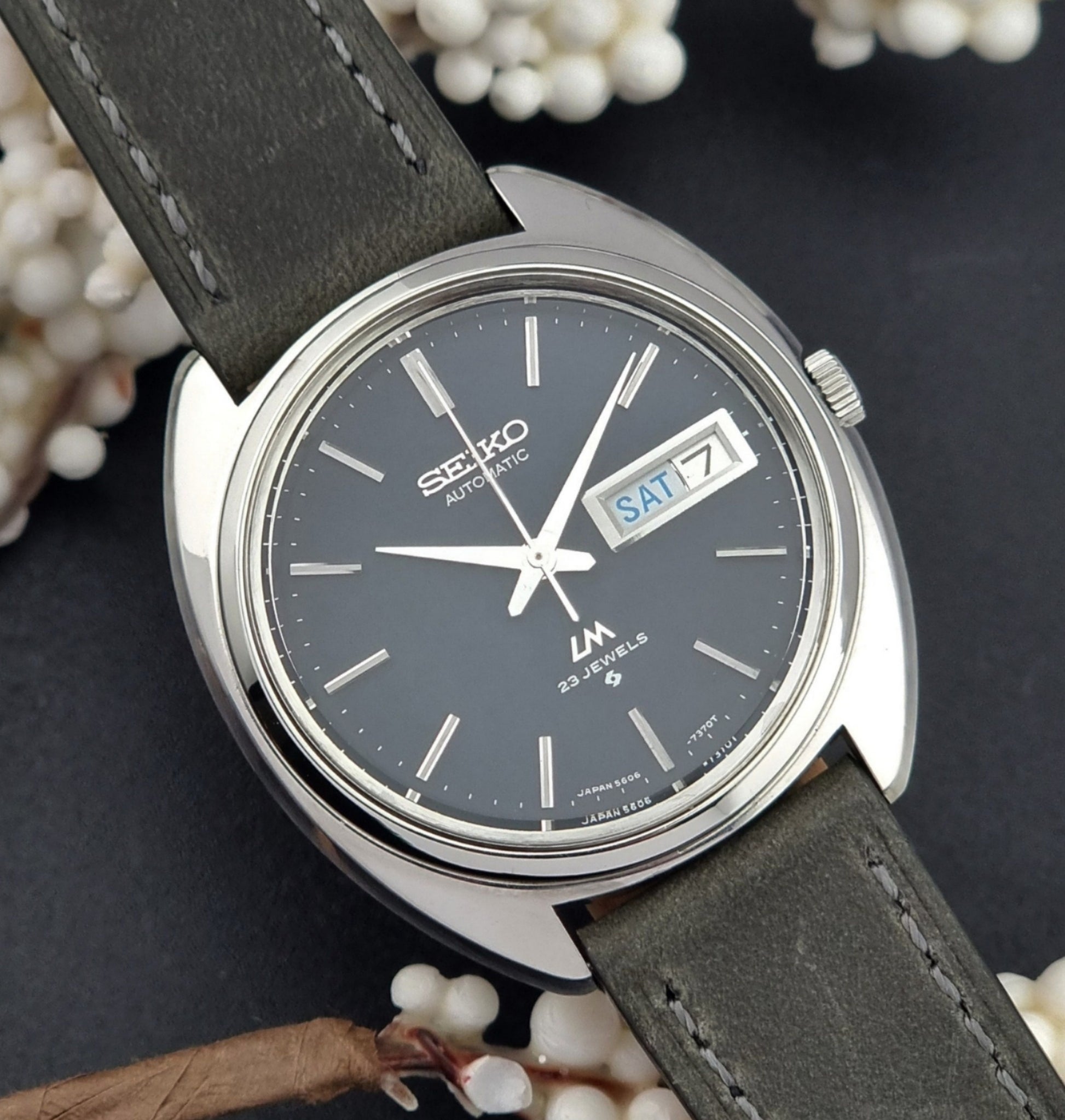 Vintage Seiko Lordmatic 5606-7150 wristwatch with a dark gray strap on a dark background close up dial view