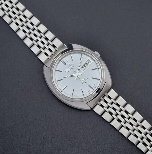 Vintage Seiko Lord Matic 5606-7150 stainless steel wristwatch with a metallic band on a dark gray background