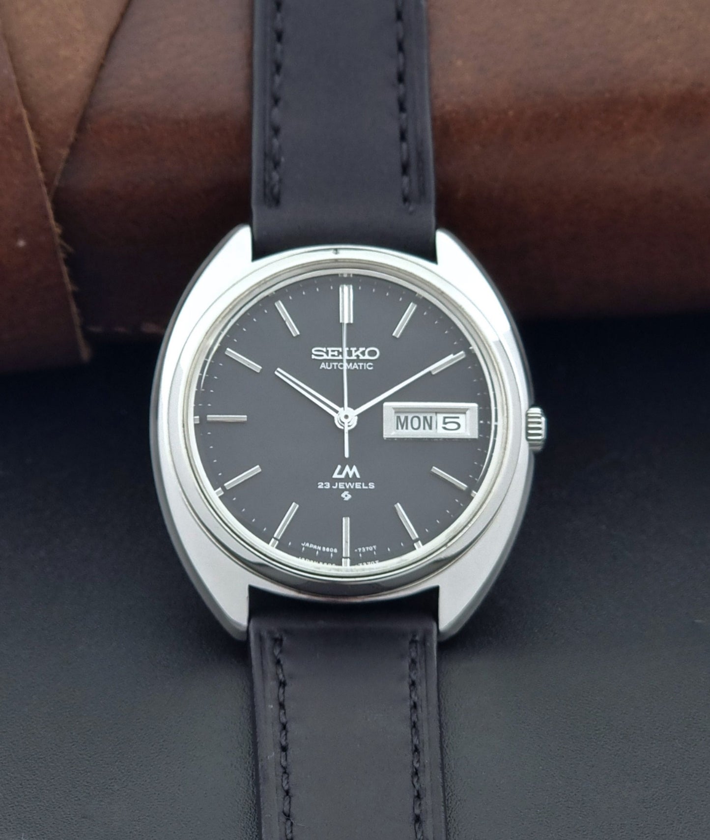 Vintage Seiko watch LordMatic 5606-7150 with black leather strap on a brown leather surface front