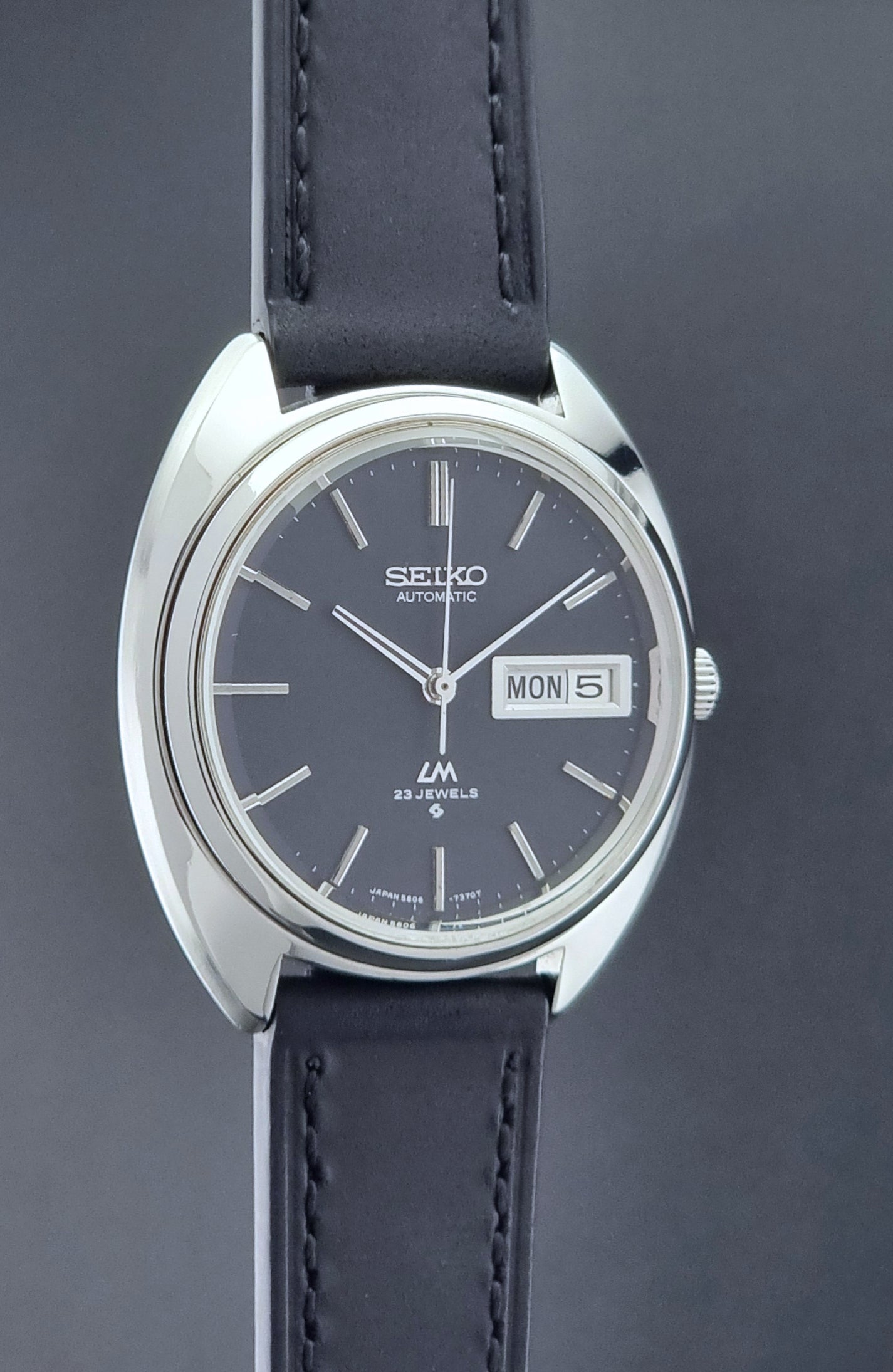 Vintage Seiko watch LordMatic 5606-7150 with black leather strap on a brown leather surface side profile