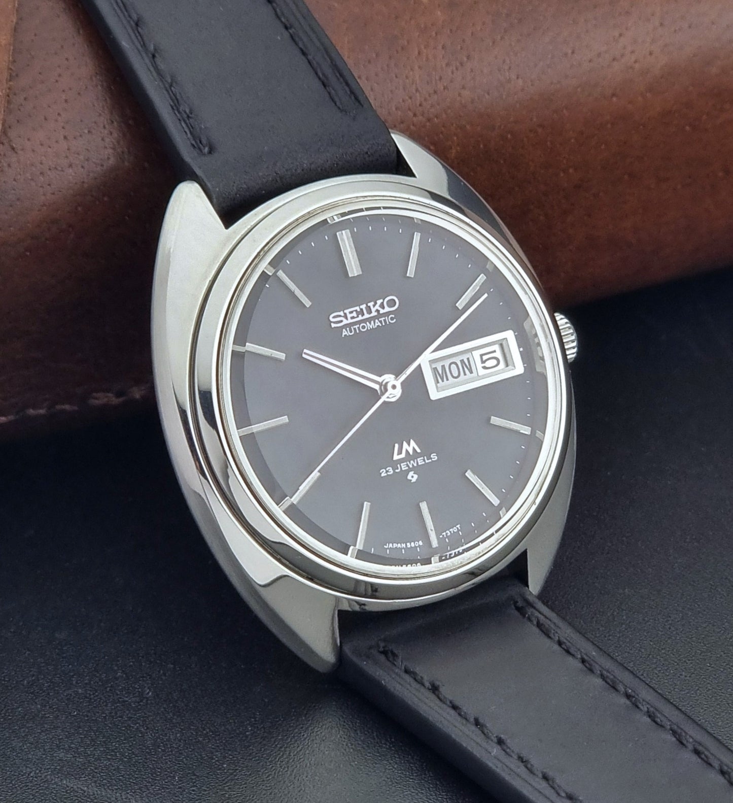Vintage Seiko watch LordMatic 5606-7150 with black leather strap on a brown leather surface side view