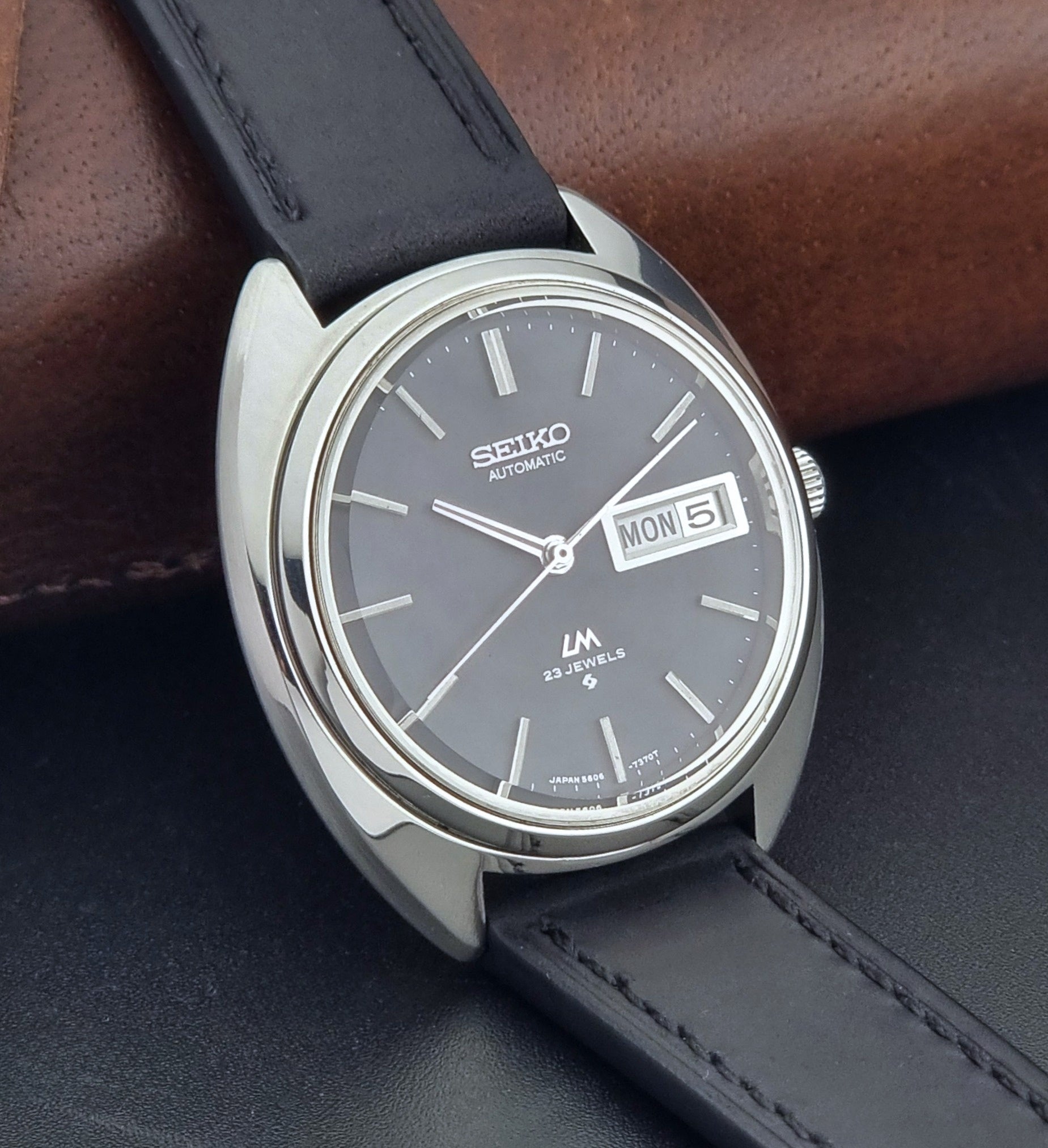 Vintage Seiko watch LordMatic 5606-7150 with black leather strap on a brown leather surface side view