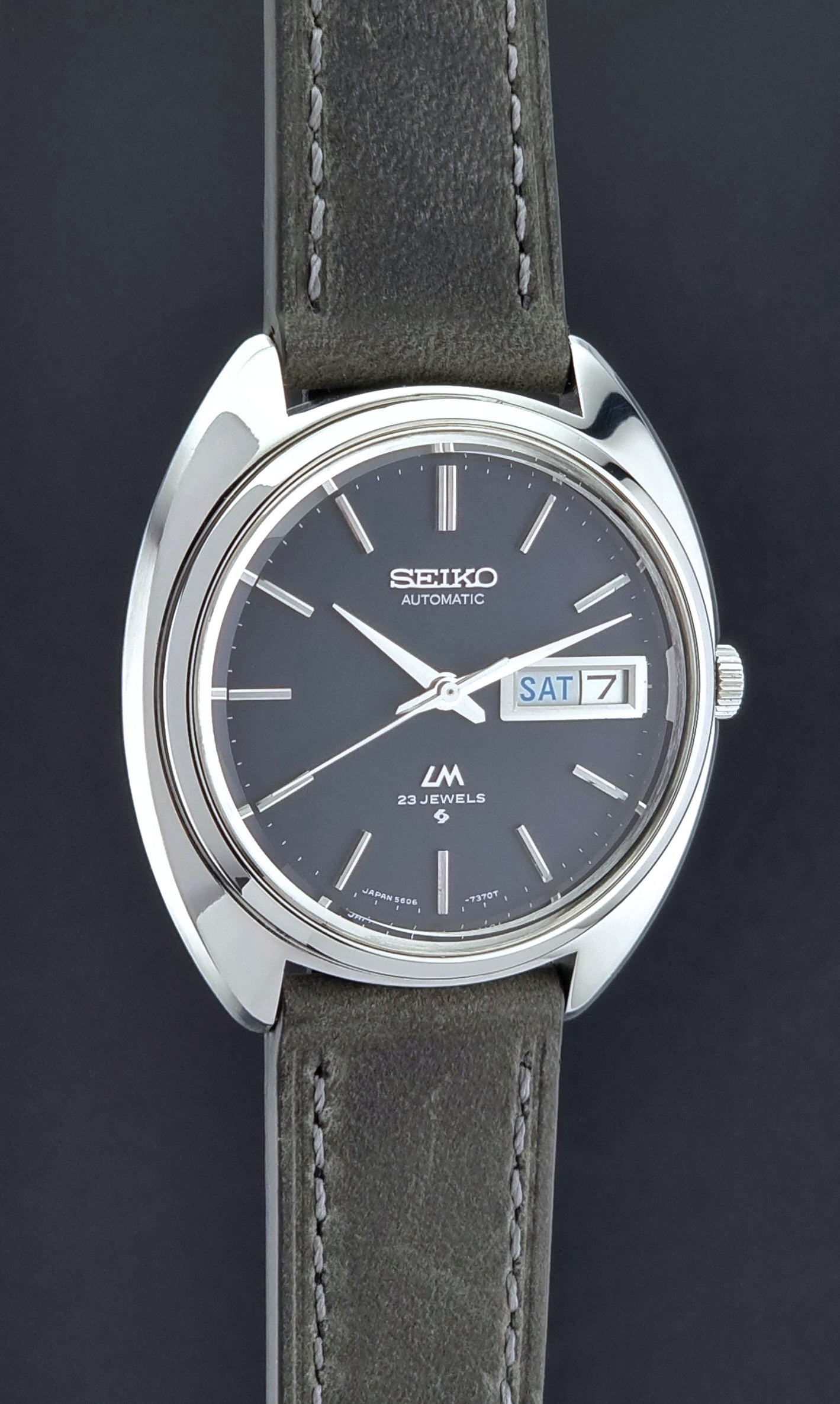 Vintage Seiko Lordmatic 5606-7150 wristwatch with a dark gray strap on a dark background  side profile view