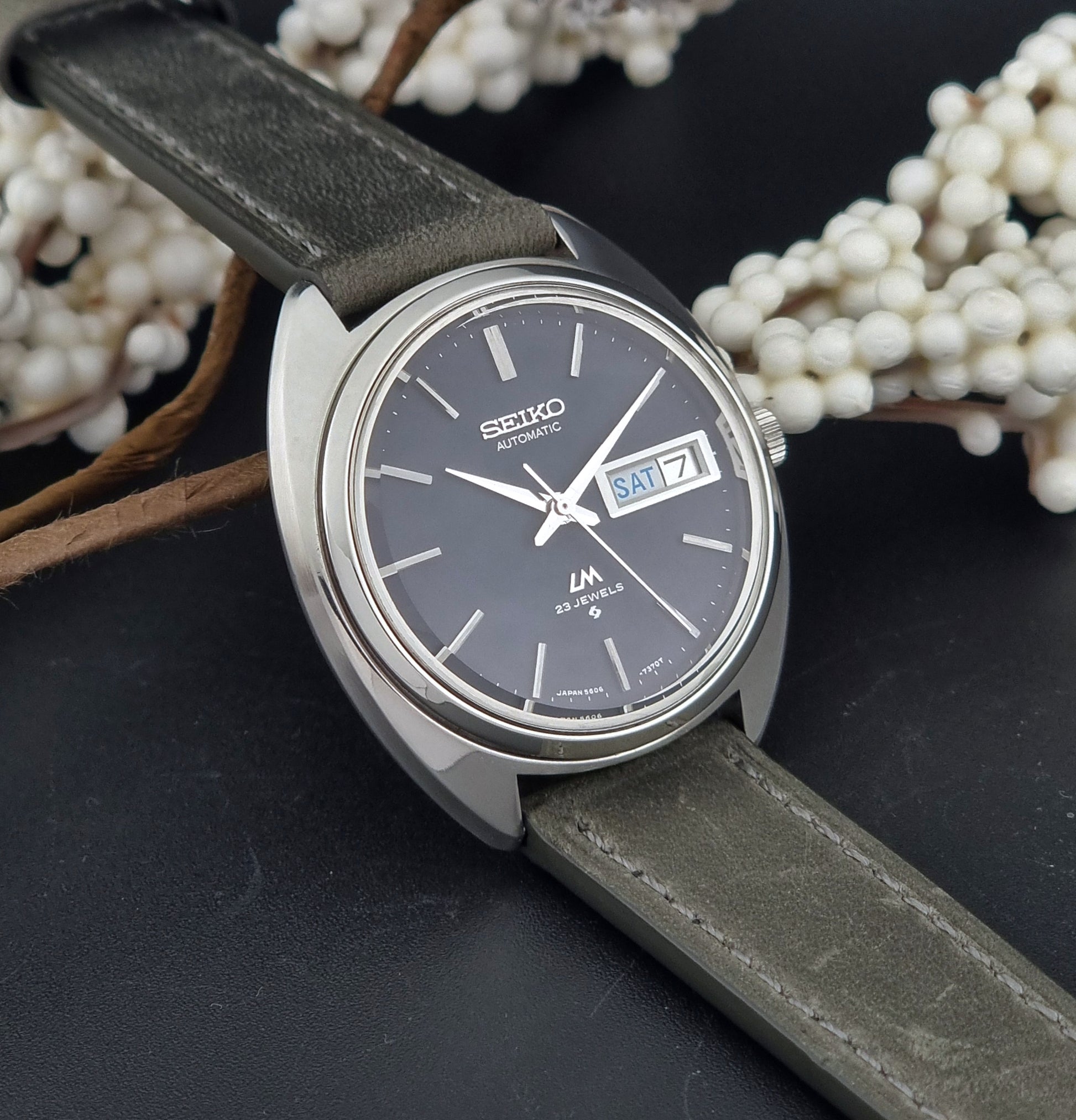 Vintage Seiko Lordmatic 5606-7150 wristwatch with a dark gray strap on a dark background side view