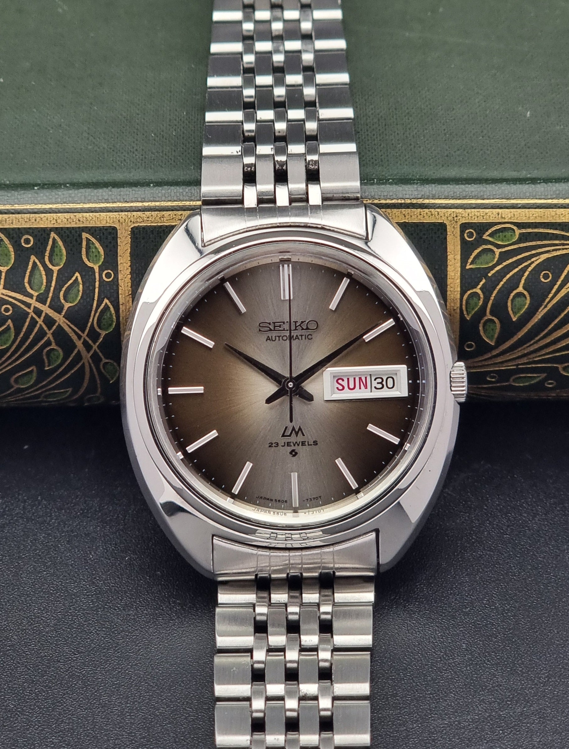 Silver Vintage Seiko Lord Matic watch with brown dial on a decorative green and gold background