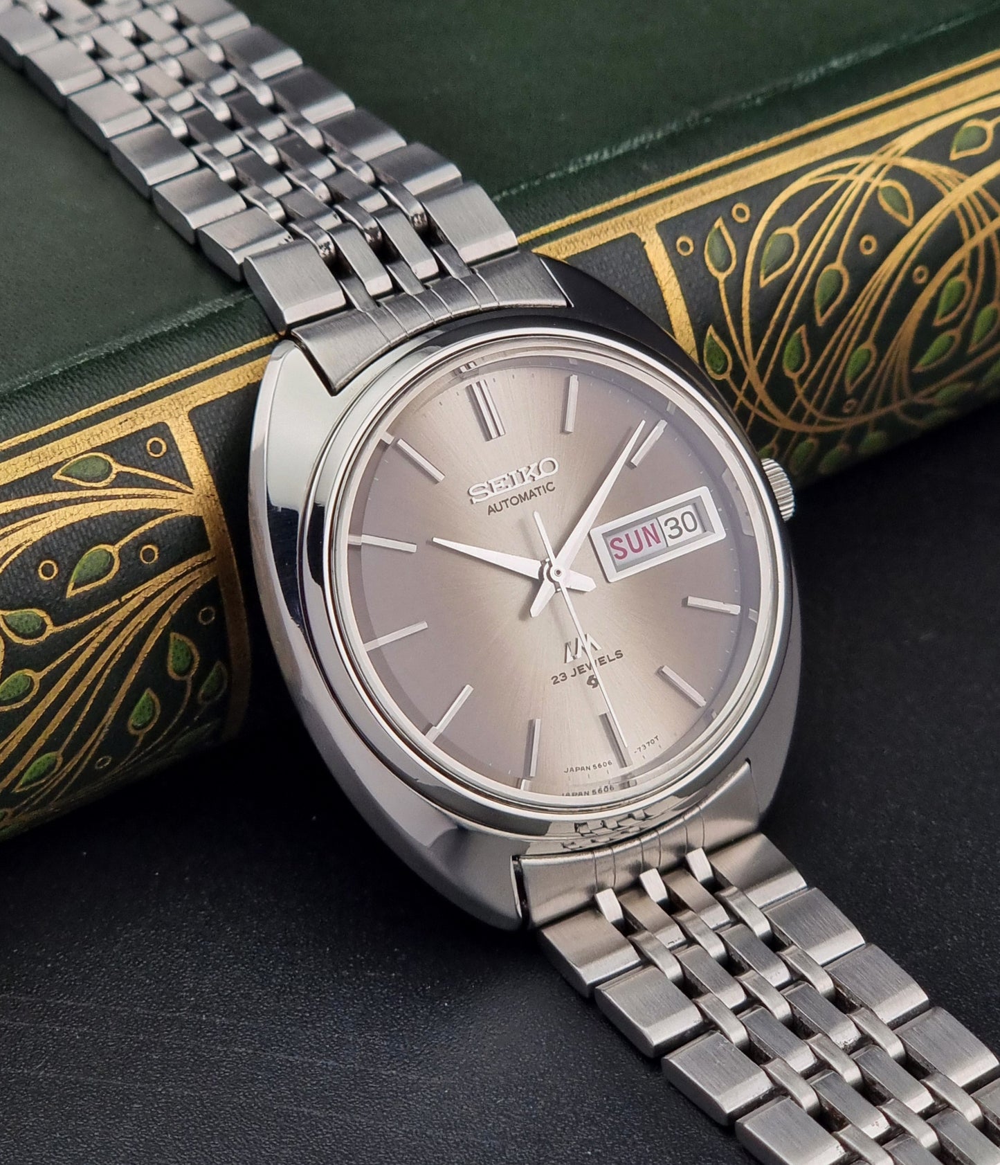 Silver Vintage Seiko Lord Matic watch on a dark surface with decorative green book