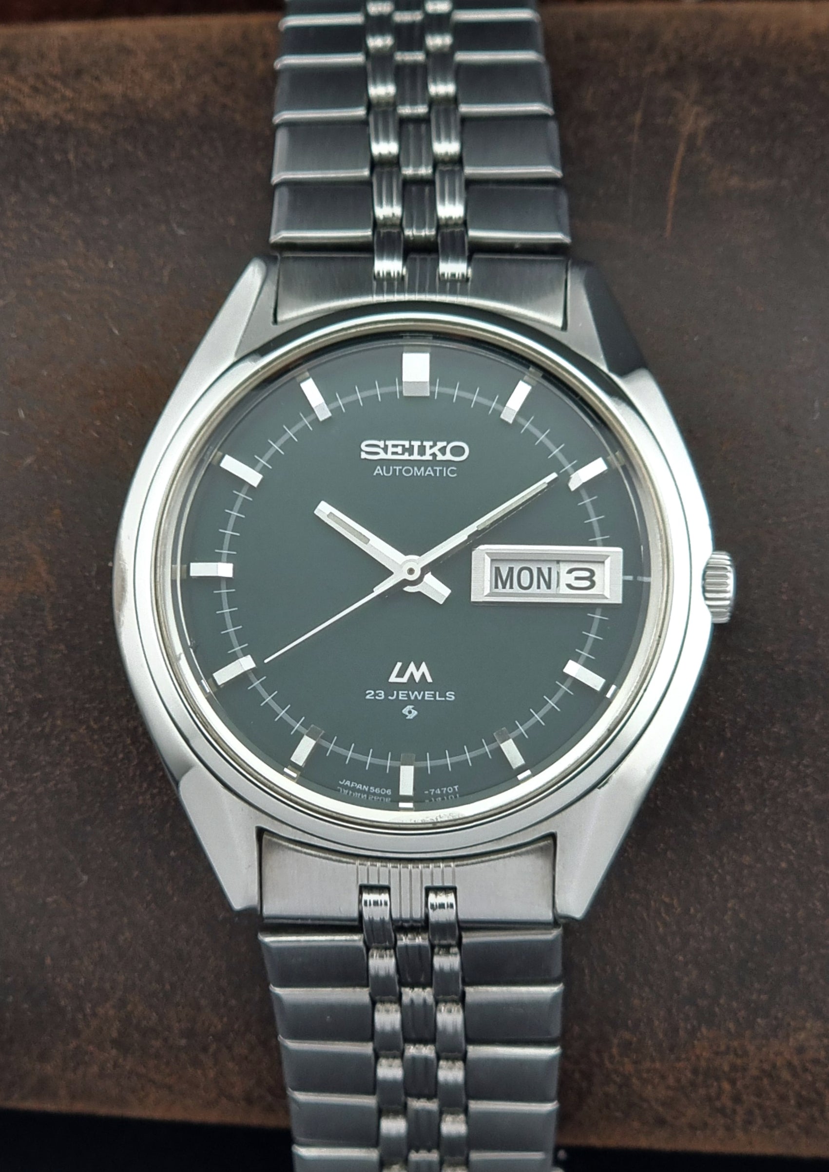 Silver Seiko watch with a dark green face on a brown leather surface