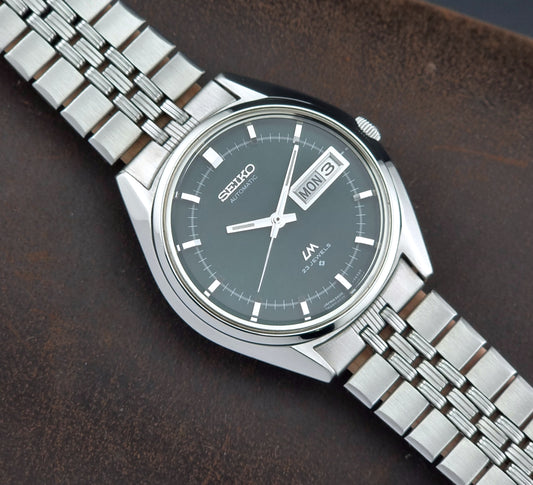 Silver Seiko watch with a dark green face on a brown leather background