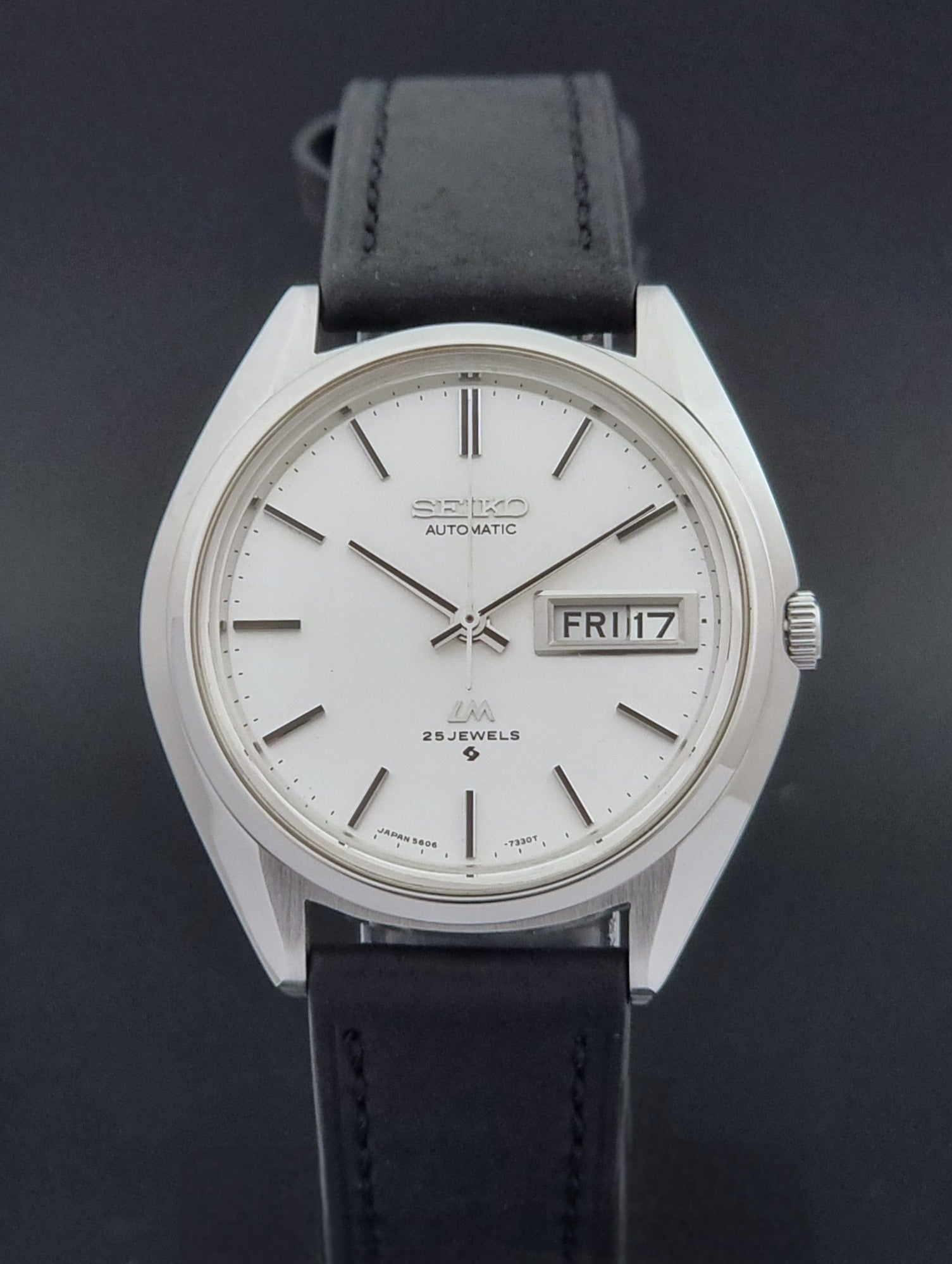 Vintage Seiko Wristwatch LordMatic 5606-7190 black strap and silver case on a dark gray background close dial view