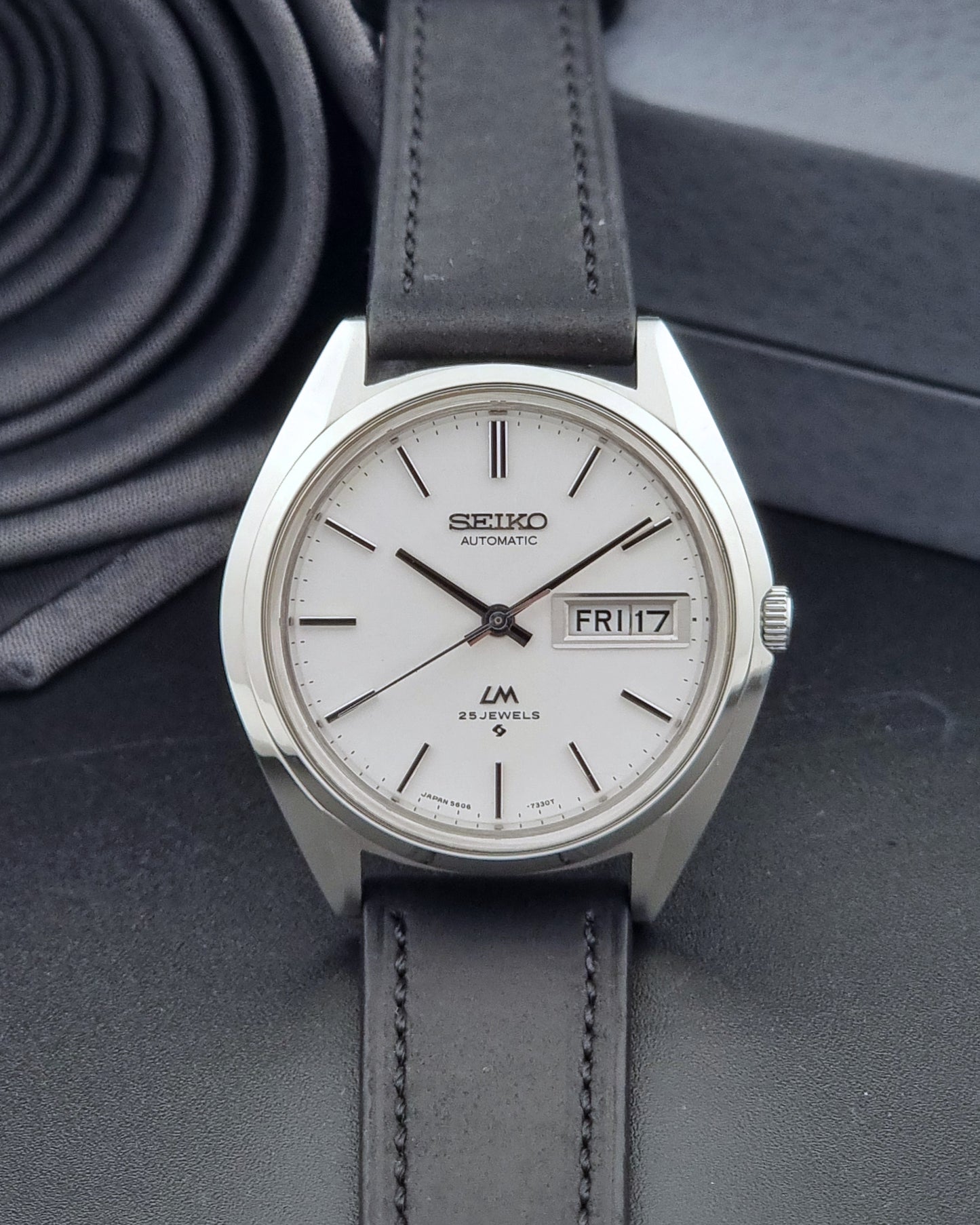 Vintage Seiko Wristwatch LordMatic 5606-7190 black strap and silver case on a dark gray background dial view
