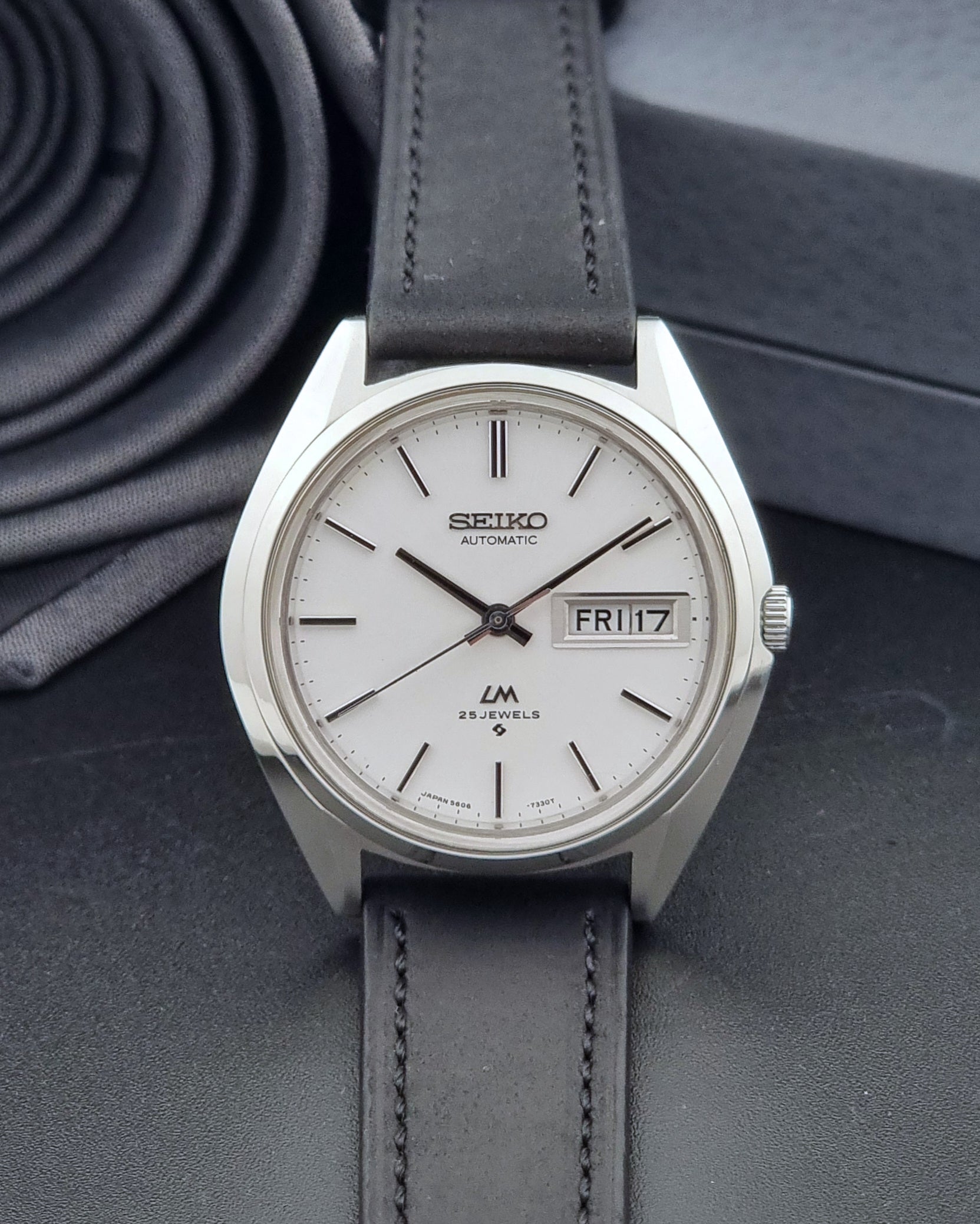 Vintage Seiko Wristwatch LordMatic 5606-7190 black strap and silver case on a dark gray background dial view