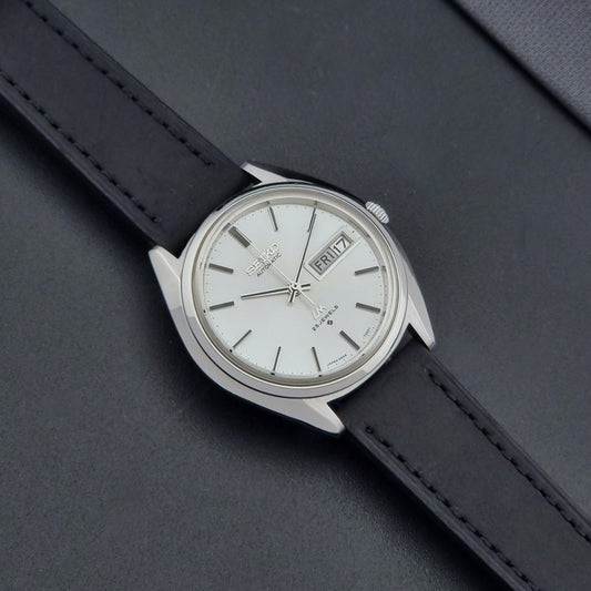 Vintage Seiko Wristwatch LordMatic 5606-7190 black strap and silver case on a dark gray background dial