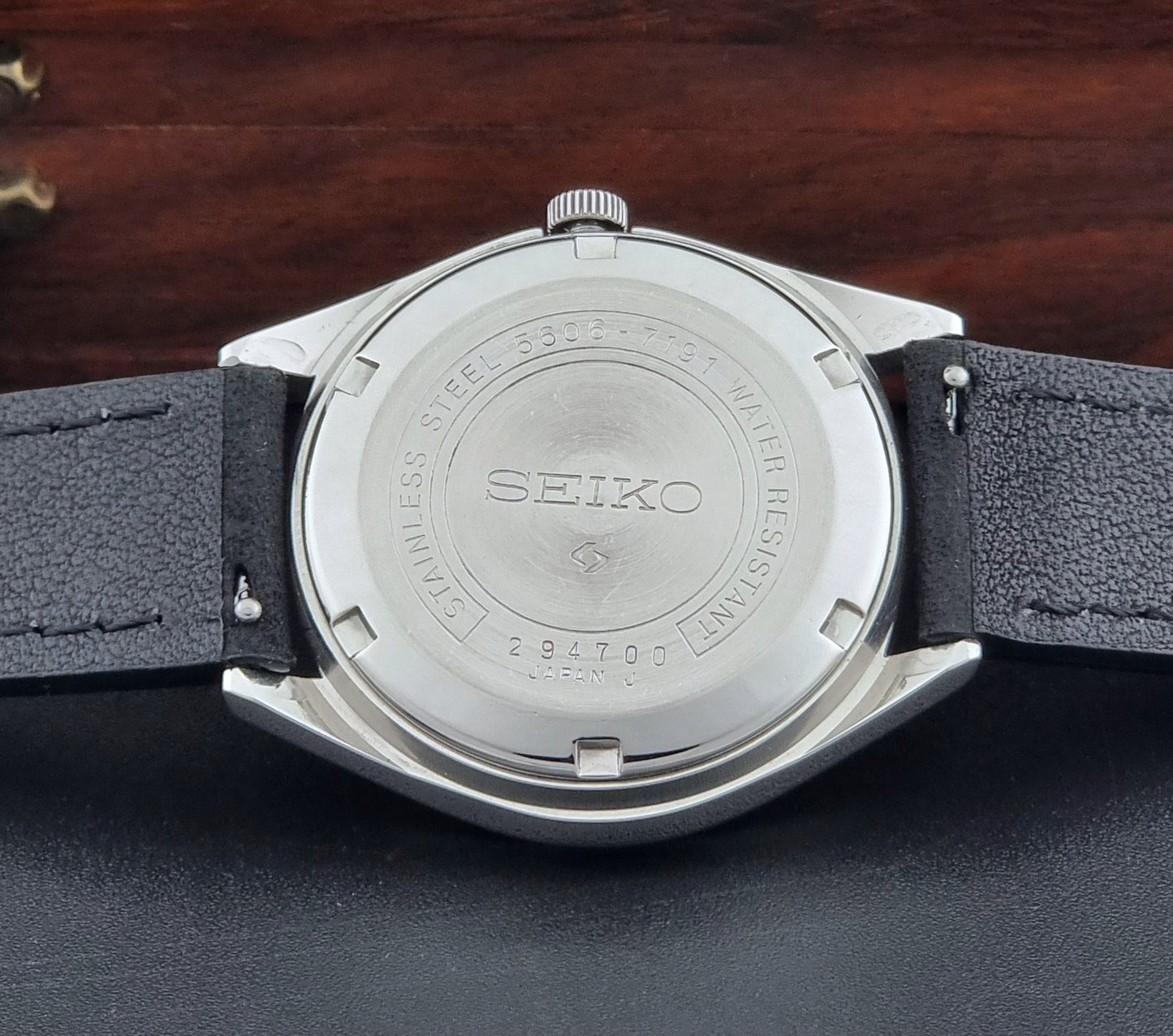 Vintage Seiko LordMatic 5606-7191 watch with a black leather strap on a dark gray background case back view
