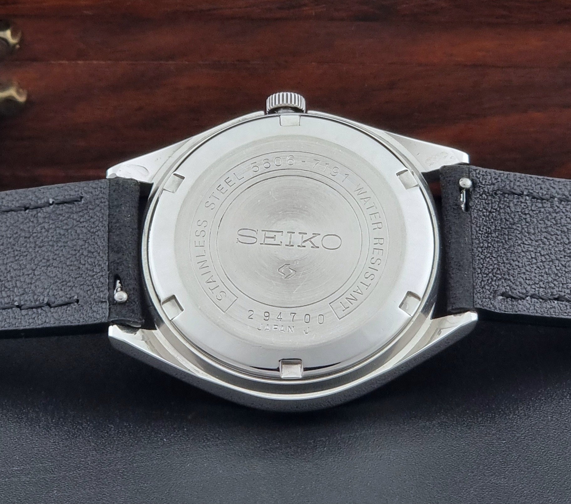 Vintage Seiko LordMatic 5606-7191 watch with a black leather strap on a dark gray background case back view