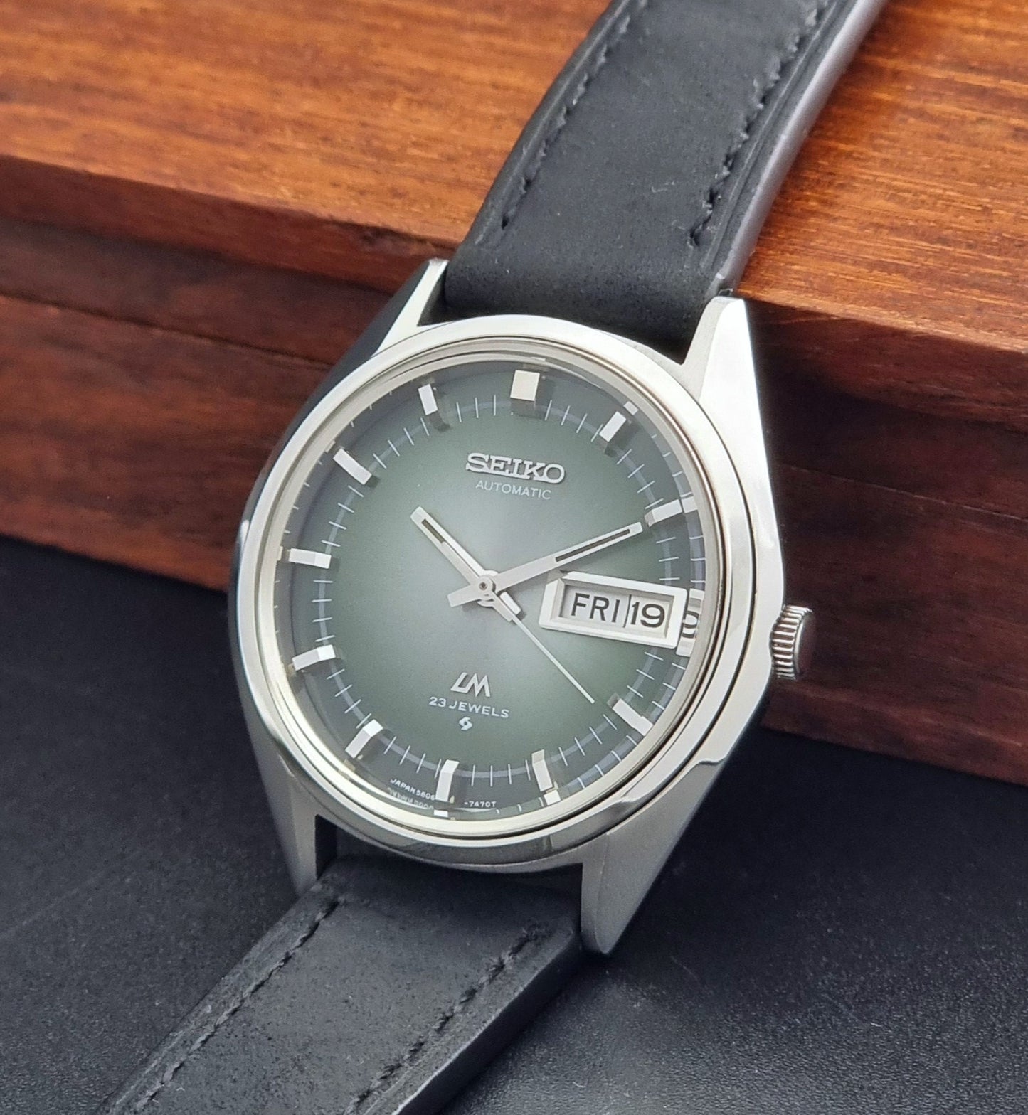 Vintage Seiko LordMatic 5606-7191 watch with a black leather strap on a dark gray background crown view