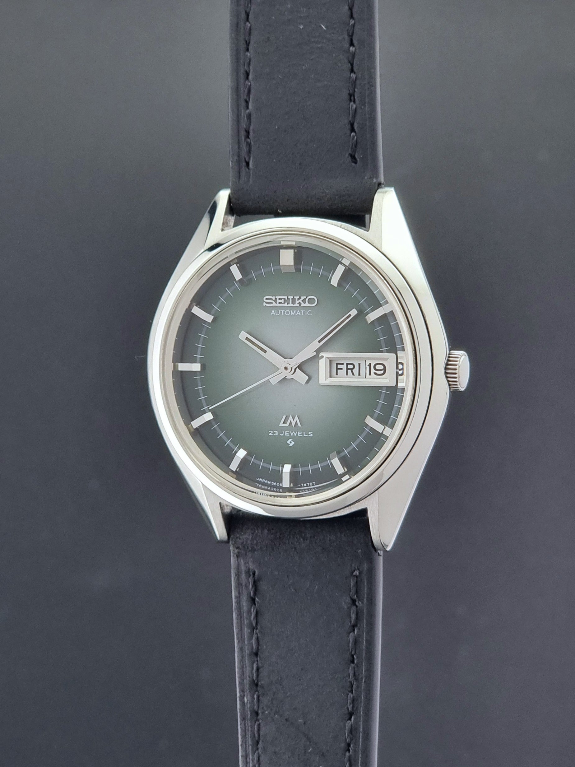 Vintage Seiko LordMatic 5606-7191 watch with a black leather strap on a dark gray background crown profile view