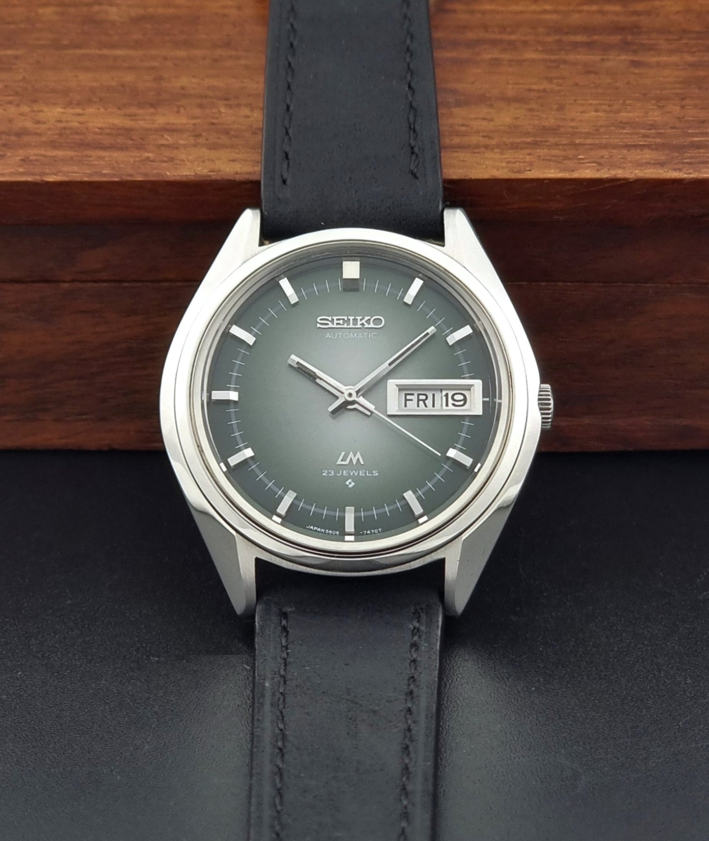 Vintage Seiko LordMatic 5606-7191 watch with a black leather strap on a dark gray background dial view