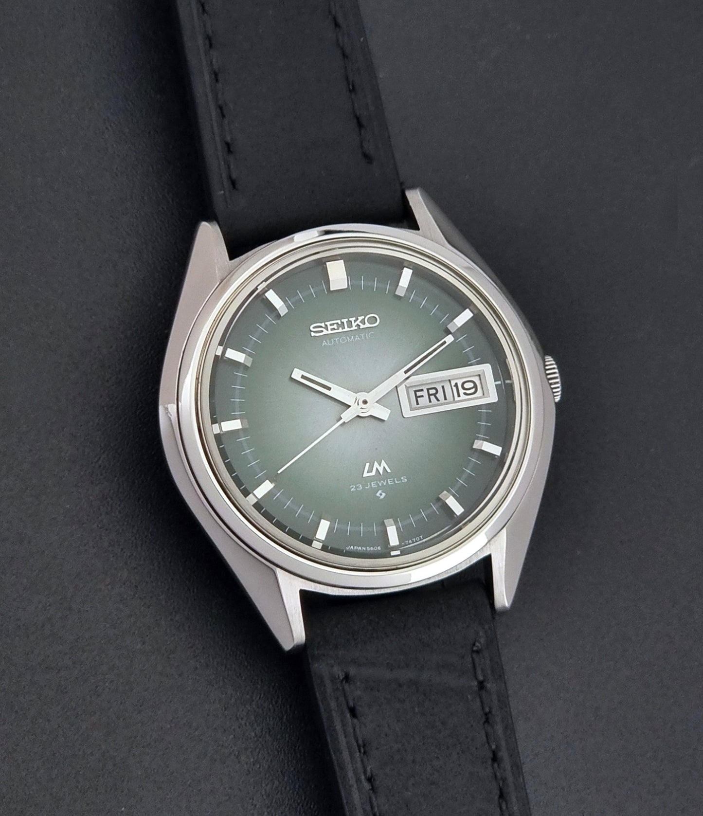 Vintage Seiko LordMatic 5606-7191 watch with a black leather strap on a dark gray background front view