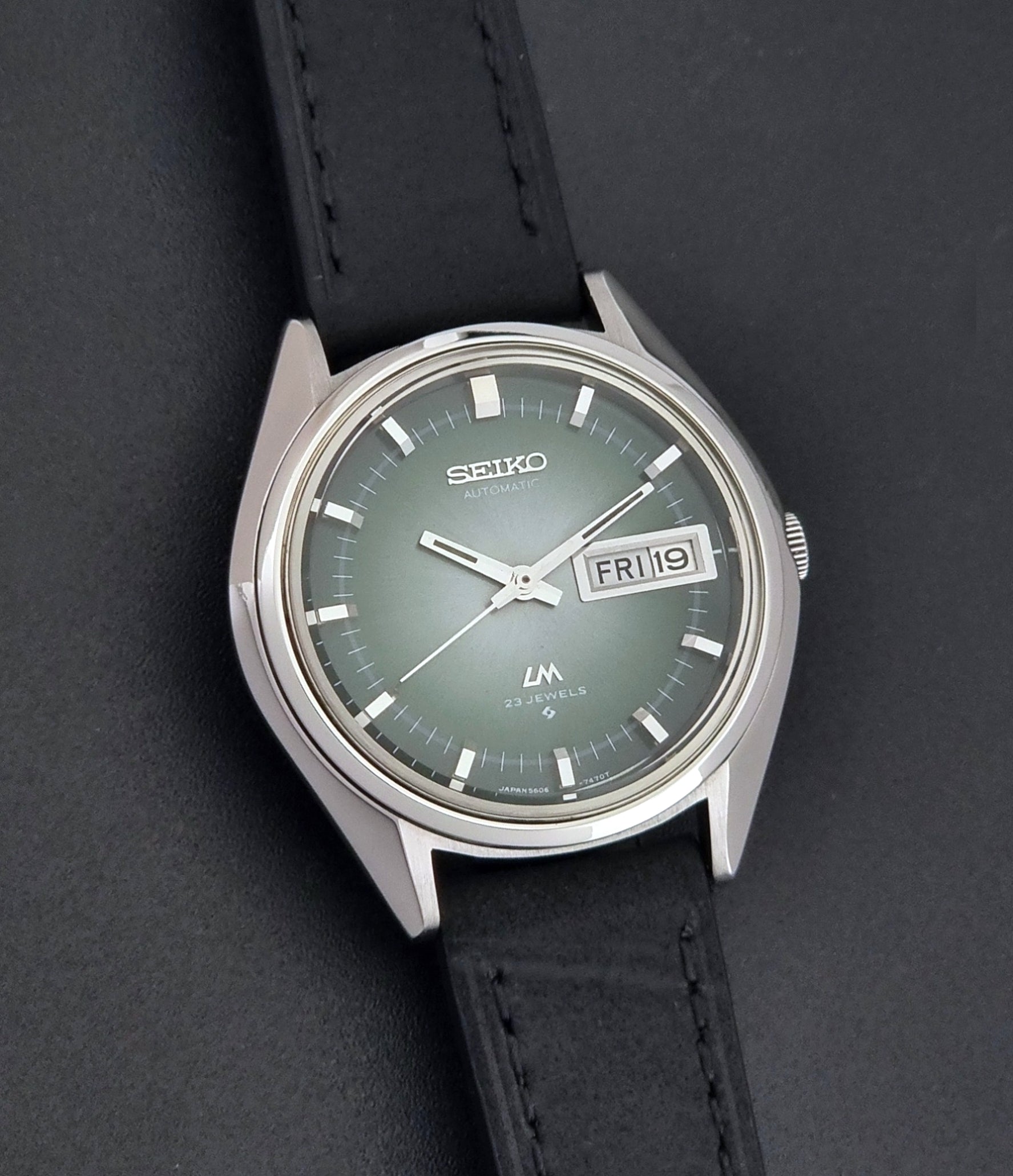 Vintage Seiko LordMatic 5606-7191 watch with a black leather strap on a dark gray background front view