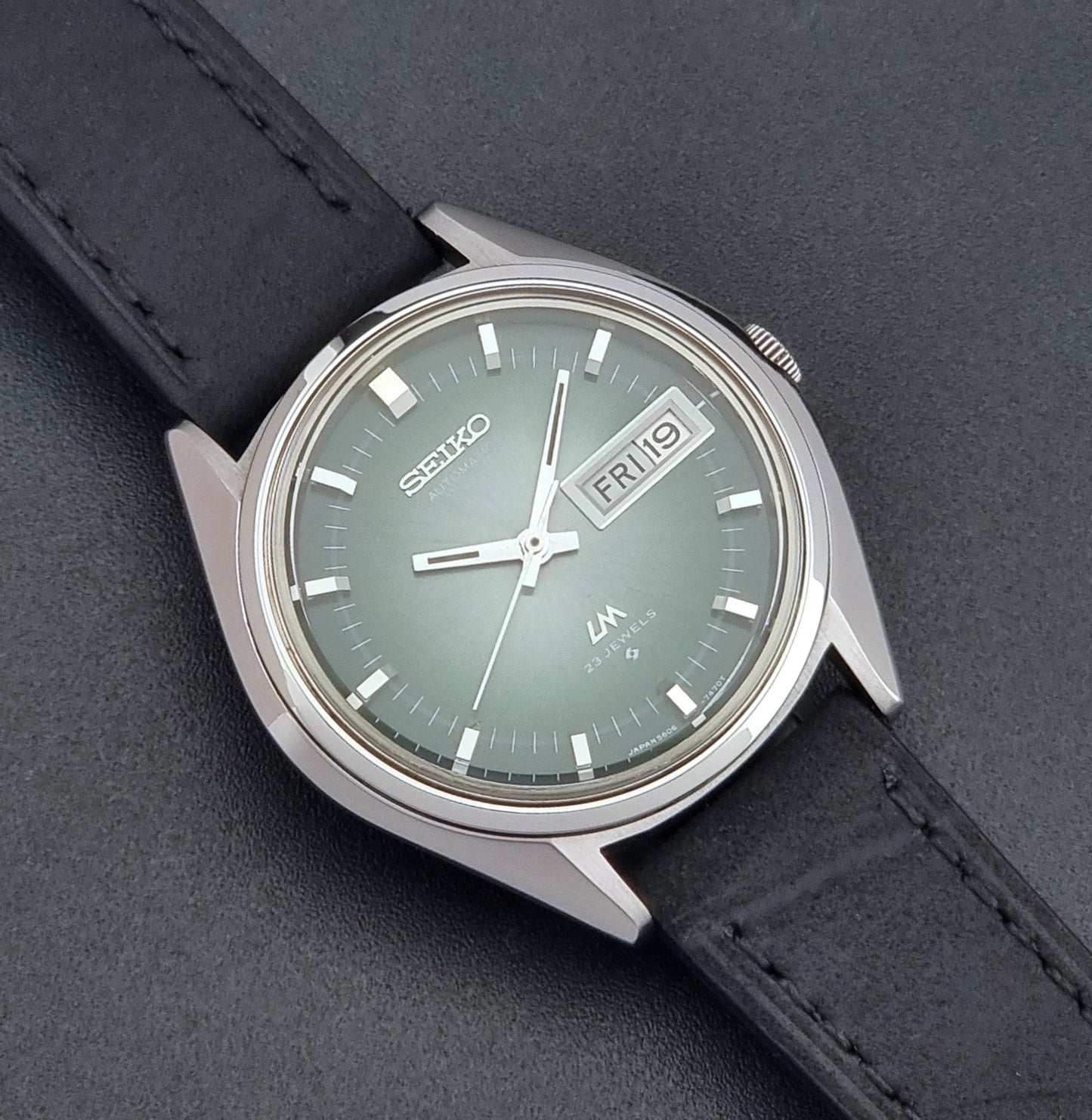Vintage Seiko LordMatic 5606-7191 watch with a black leather strap on a dark gray background close up dial view
