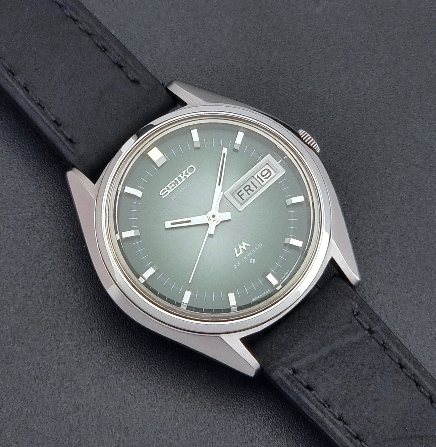 Vintage Seiko LordMatic 5606-7191 watch with a black leather strap on a dark gray background close up dial view