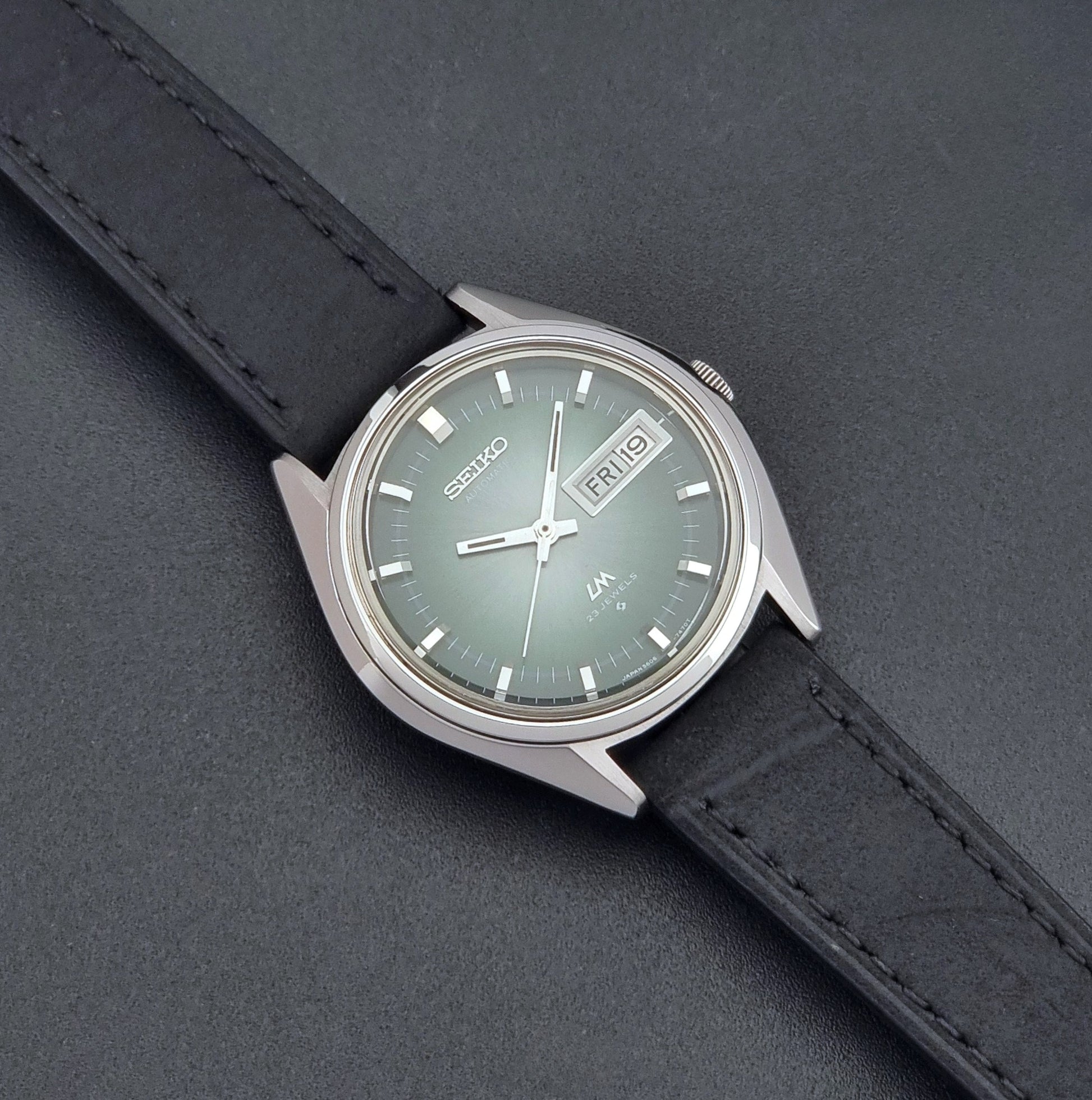 Vintage Seiko LordMatic 5606-7191 watch with a black leather strap on a dark gray background dial
