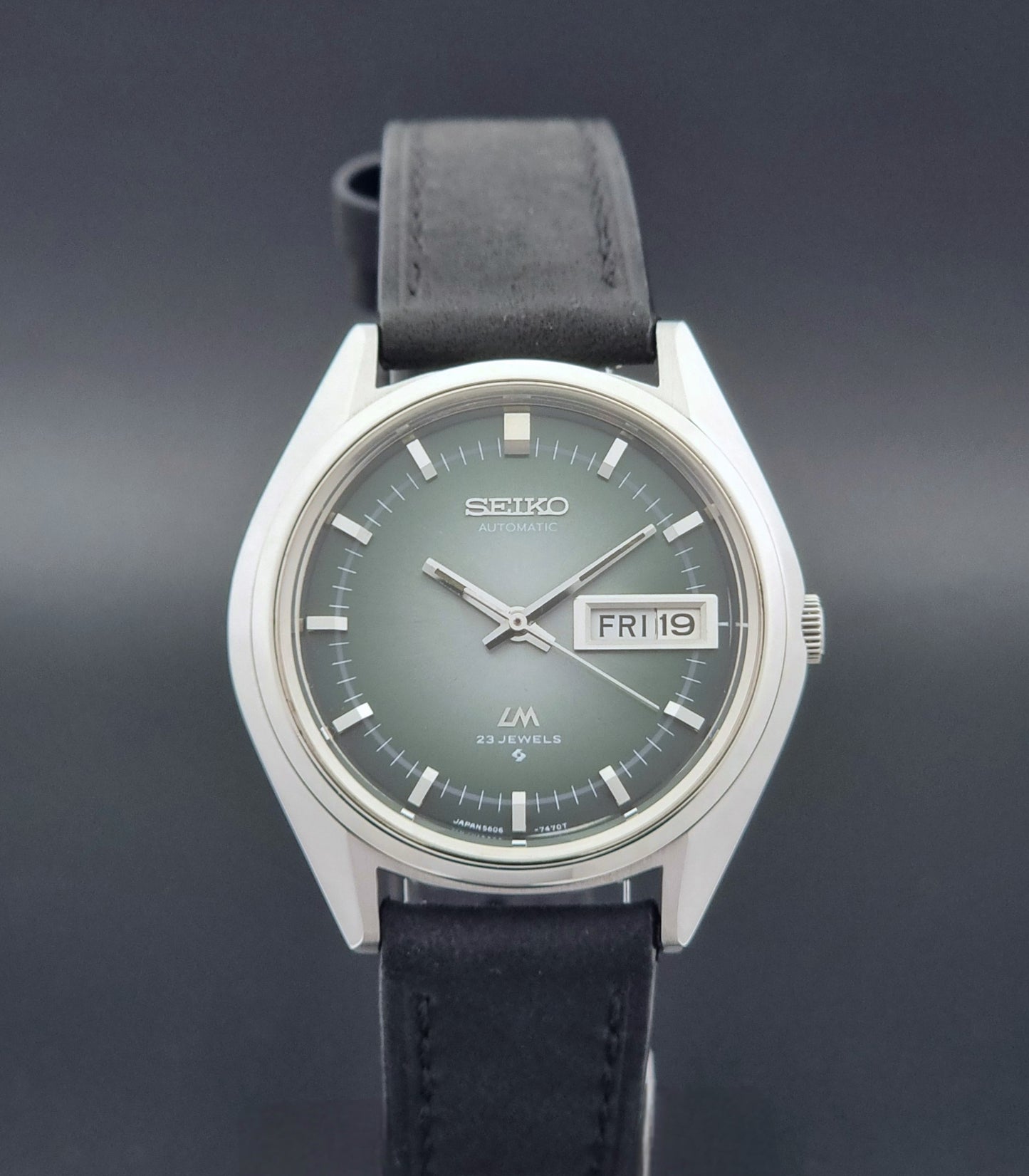 Vintage Seiko LordMatic 5606-7191 watch with a black leather strap on a dark gray background close dial view