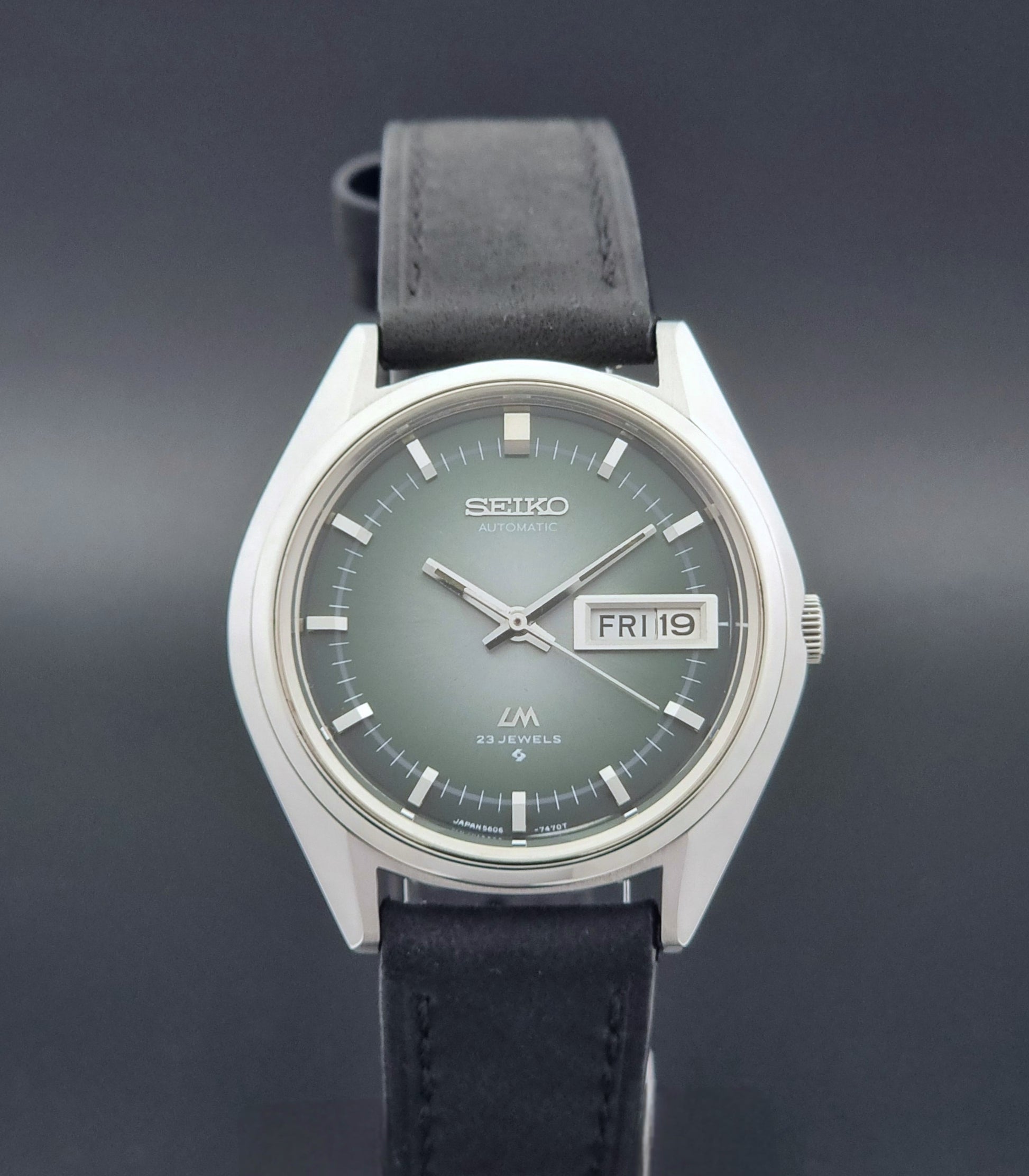 Vintage Seiko LordMatic 5606-7191 watch with a black leather strap on a dark gray background close dial view