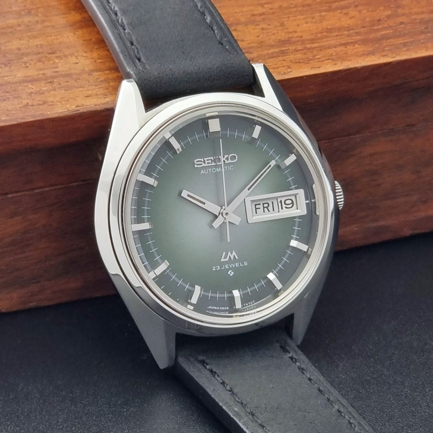 Vintage Seiko LordMatic 5606-7191 watch with a black leather strap on a dark gray background side view