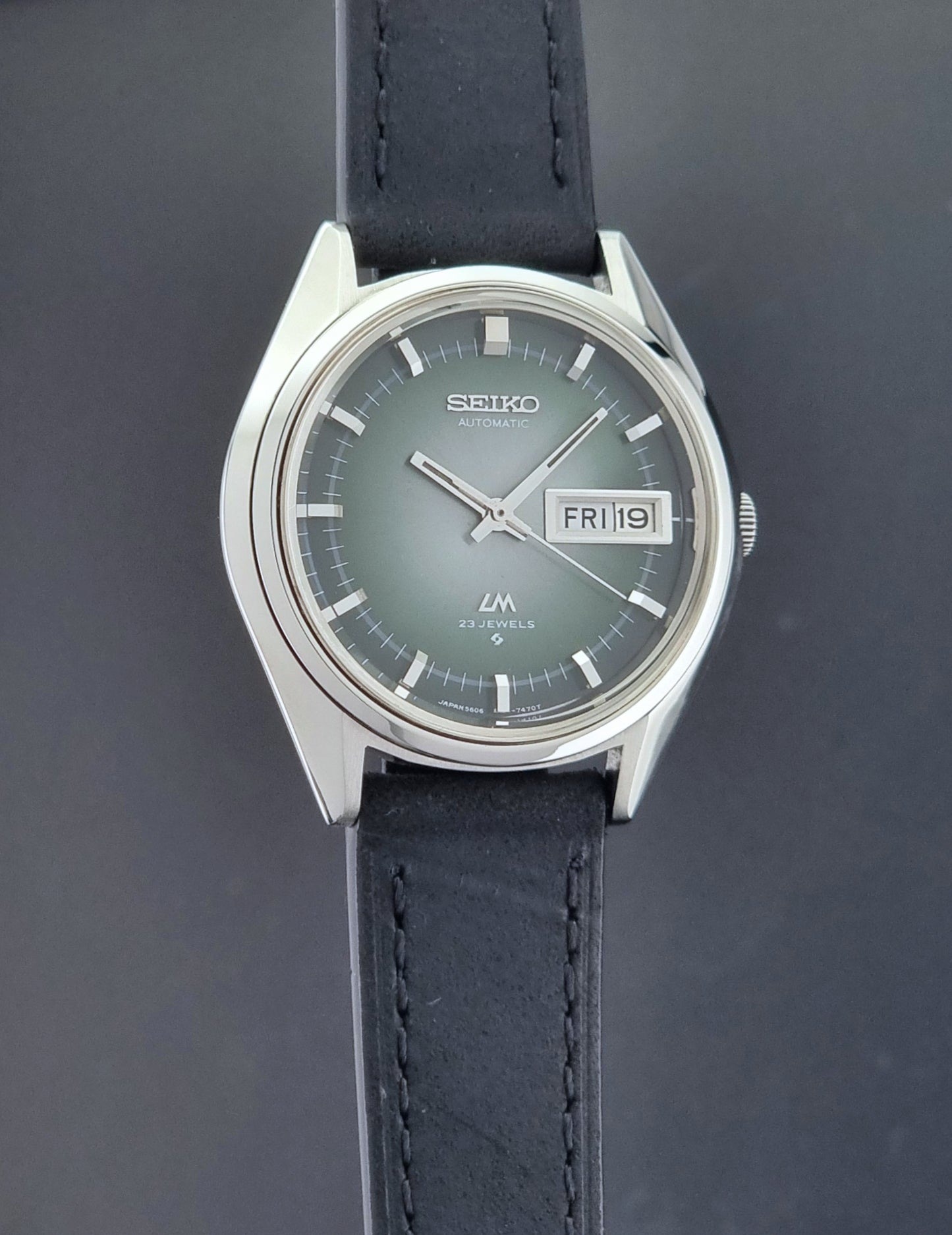 Vintage Seiko LordMatic 5606-7191 watch with a black leather strap on a dark gray background side profiel view