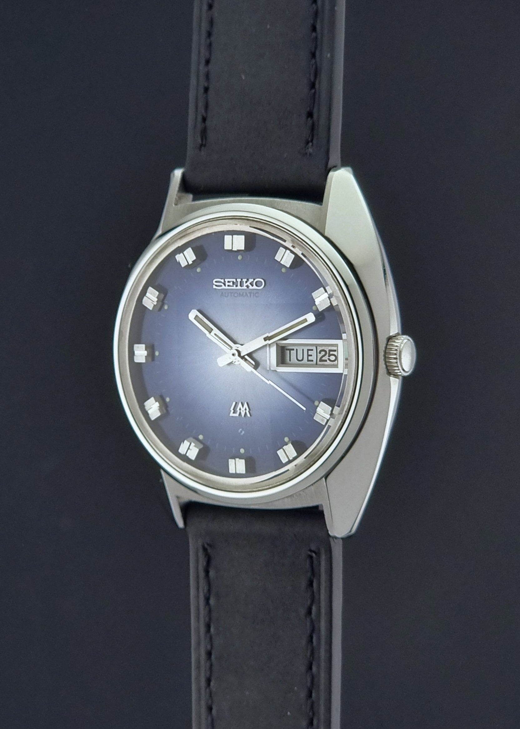 Vintage Seiko Wristwatch 5606-7231 LordMatic black strap and blue dial on a gray background crown profile view