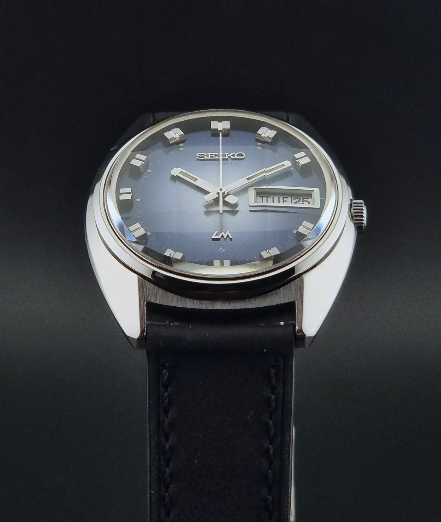 Vintage Seiko Wristwatch 5606-7231 LordMatic black strap and blue dial on a gray background crystal view