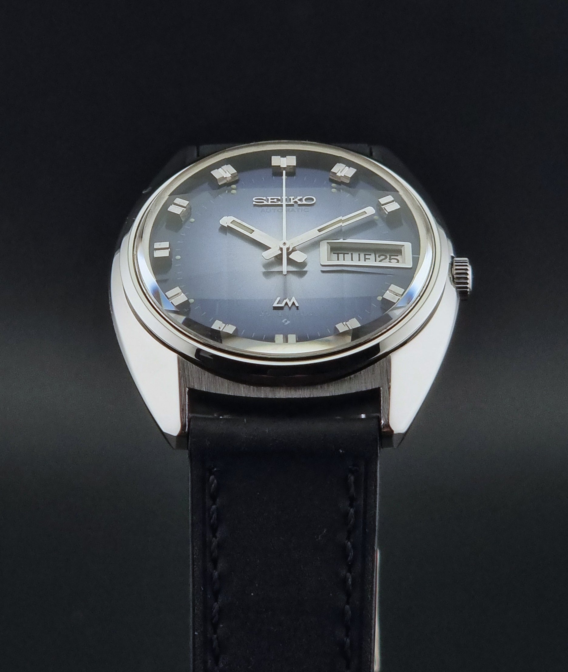 Vintage Seiko Wristwatch 5606-7231 LordMatic black strap and blue dial on a gray background crystal view