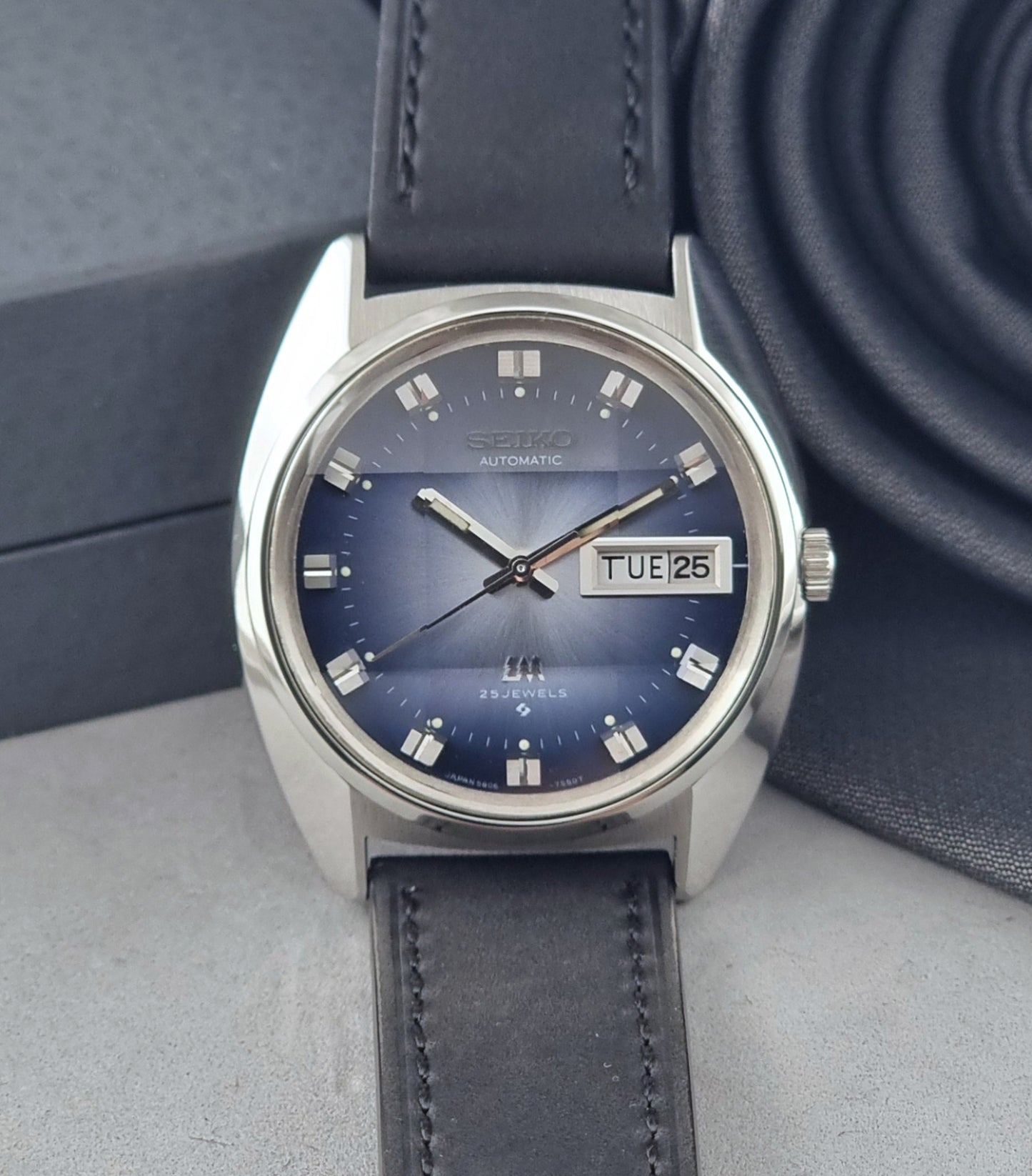 Vintage Seiko Wristwatch 5606-7231 LordMatic black strap and blue dial on a gray background dial view