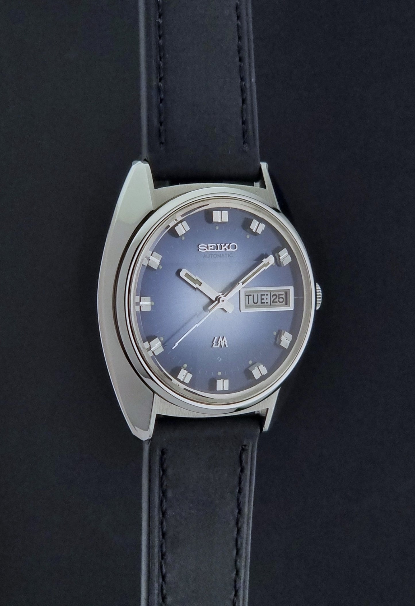 Vintage Seiko Wristwatch 5606-7231 LordMatic black strap and blue dial on a gray background side profile view