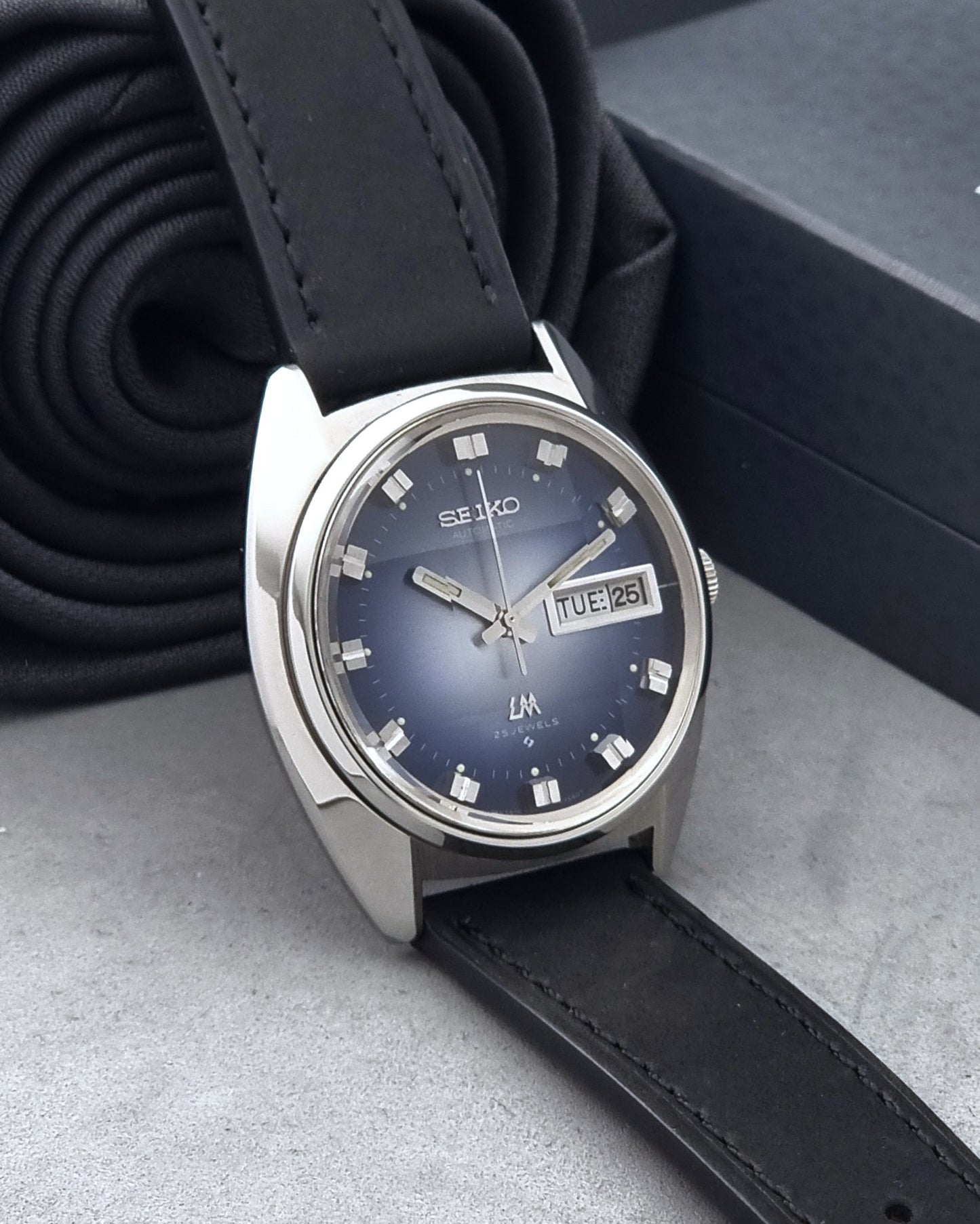 Vintage Seiko Wristwatch 5606-7231 LordMatic black strap and blue dial on a gray background side view