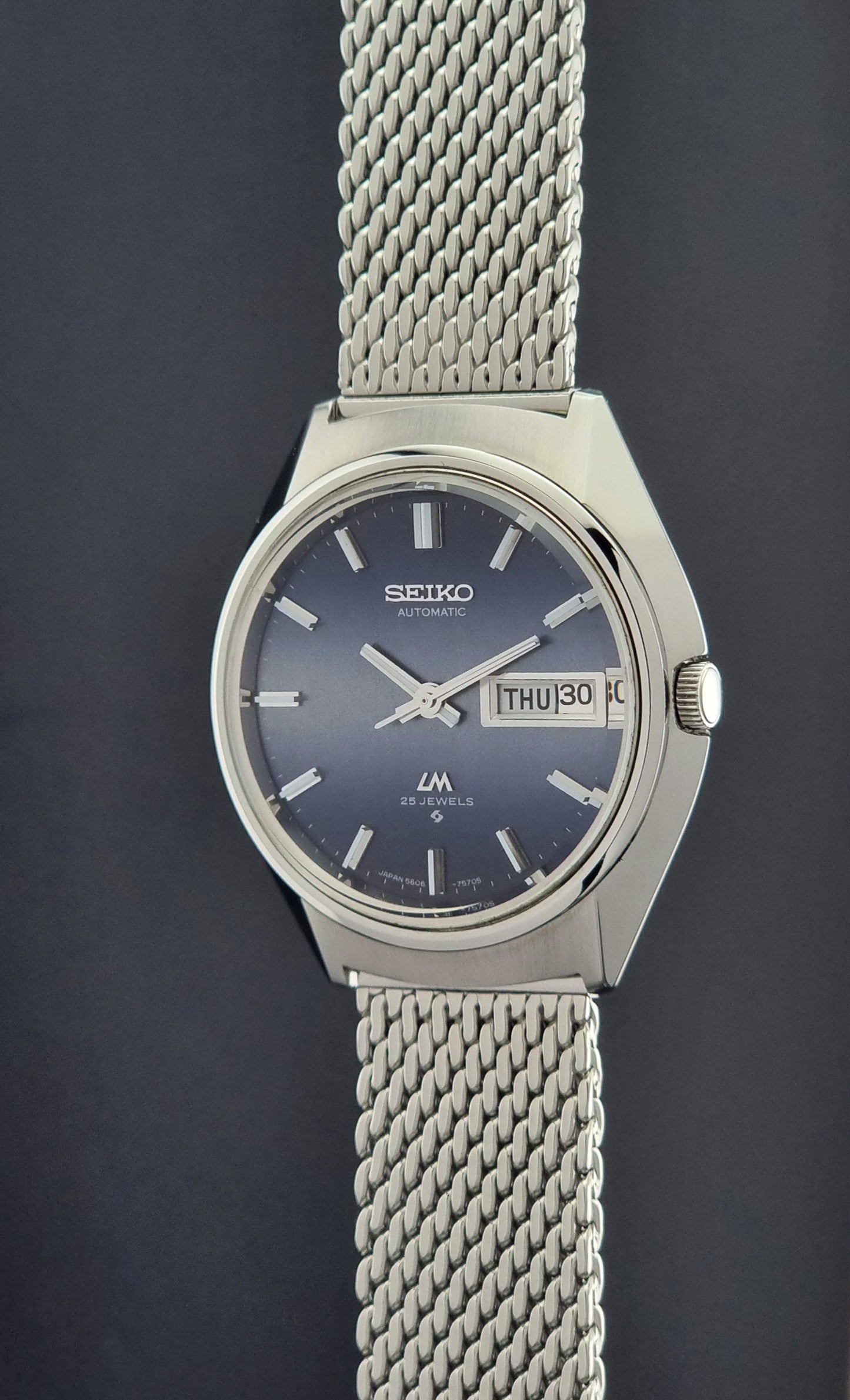 Seiko watch with blue face and mesh band on a dark background