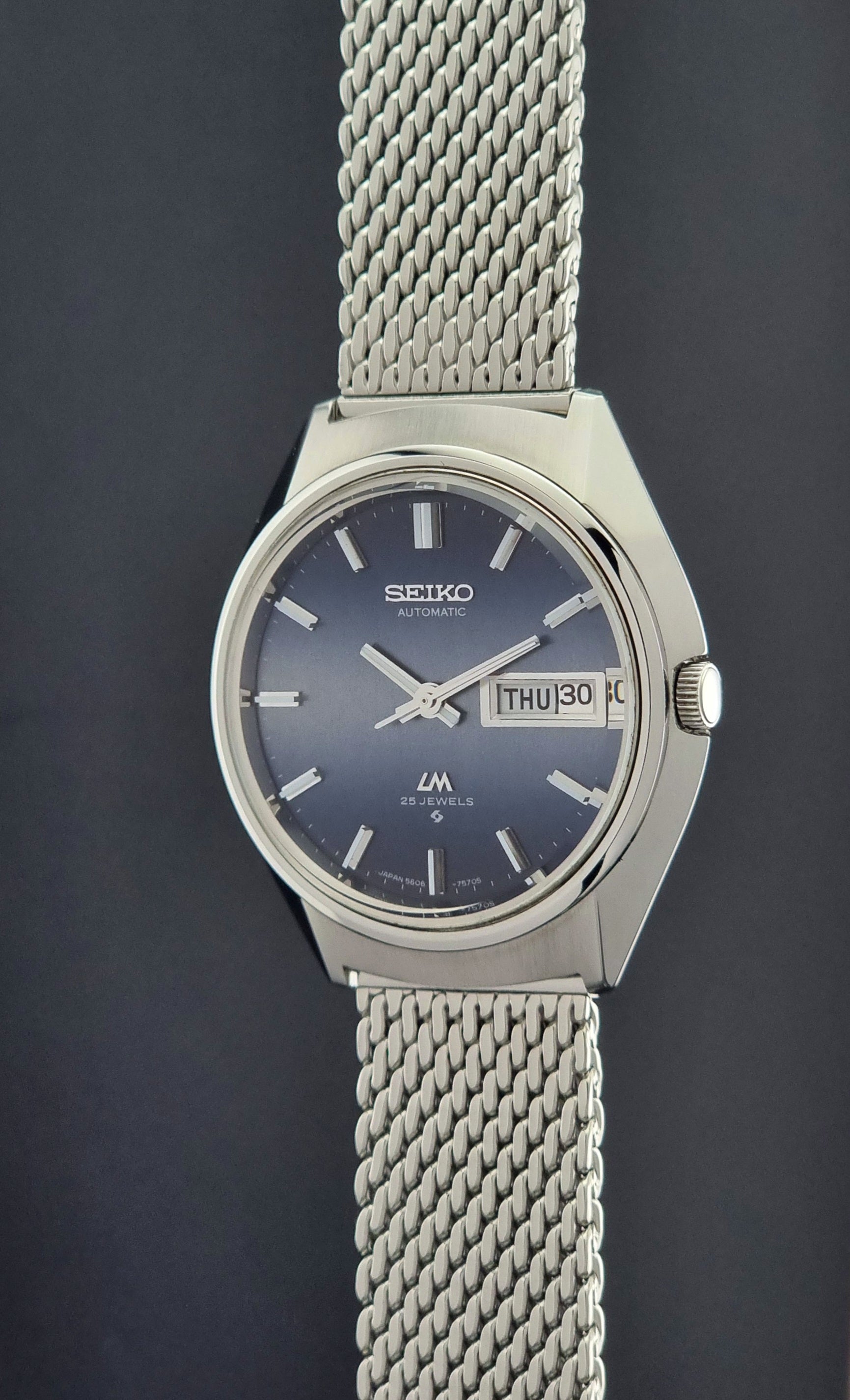 Seiko watch with blue face and mesh band on a dark background