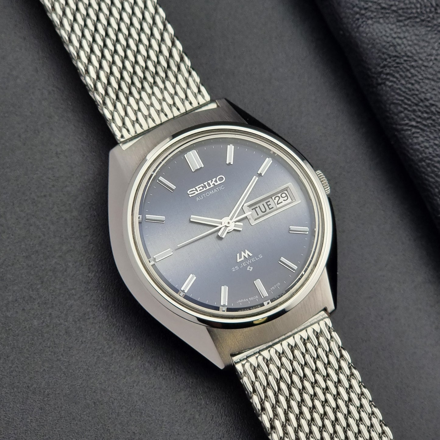 Silver Seiko watch with a mesh band on a dark background