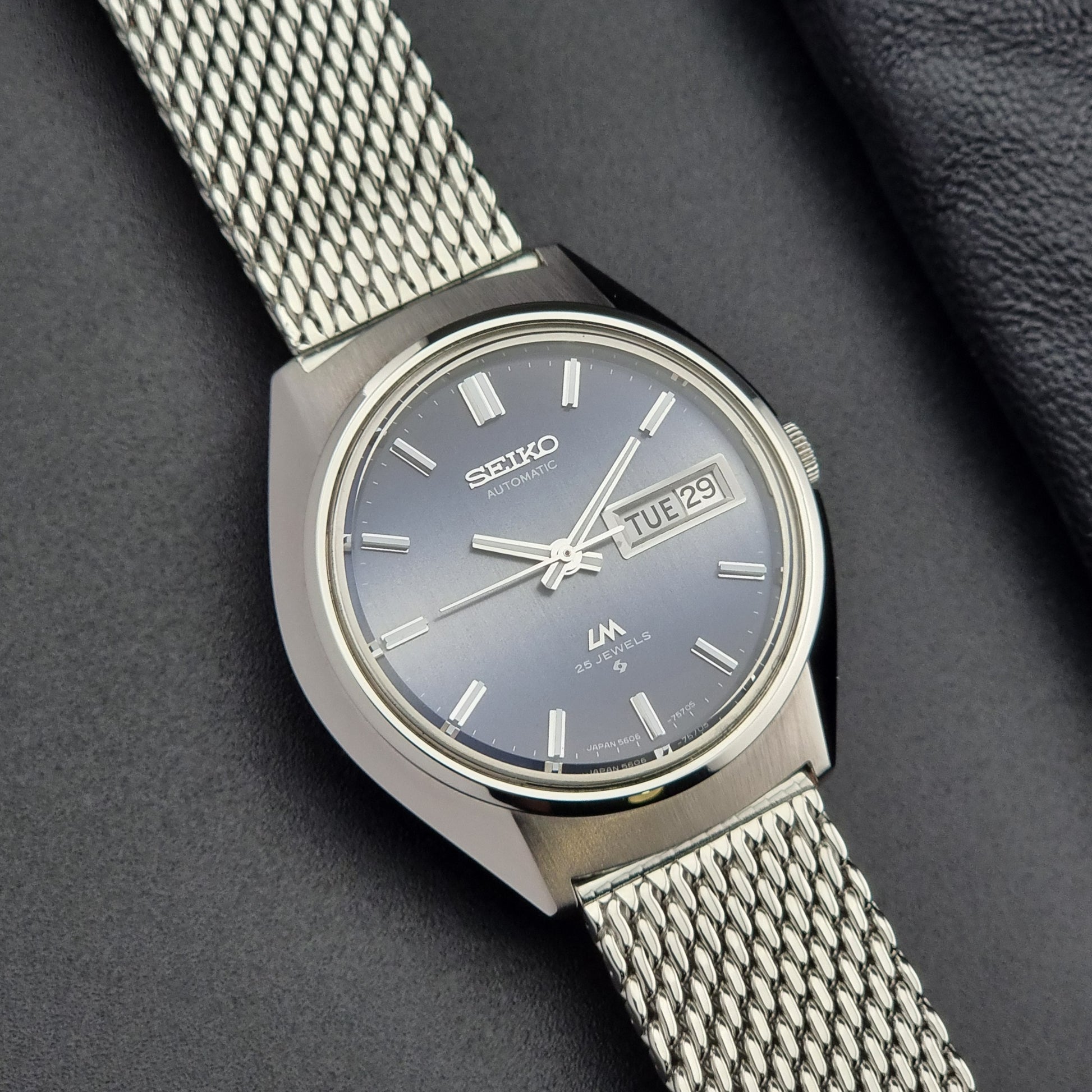 Silver Seiko watch with a mesh band on a dark background