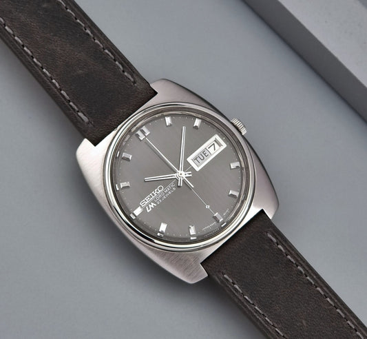 Vintage Seiko Lord Matic 5606-8010 watch with grey leather strap on a gray background