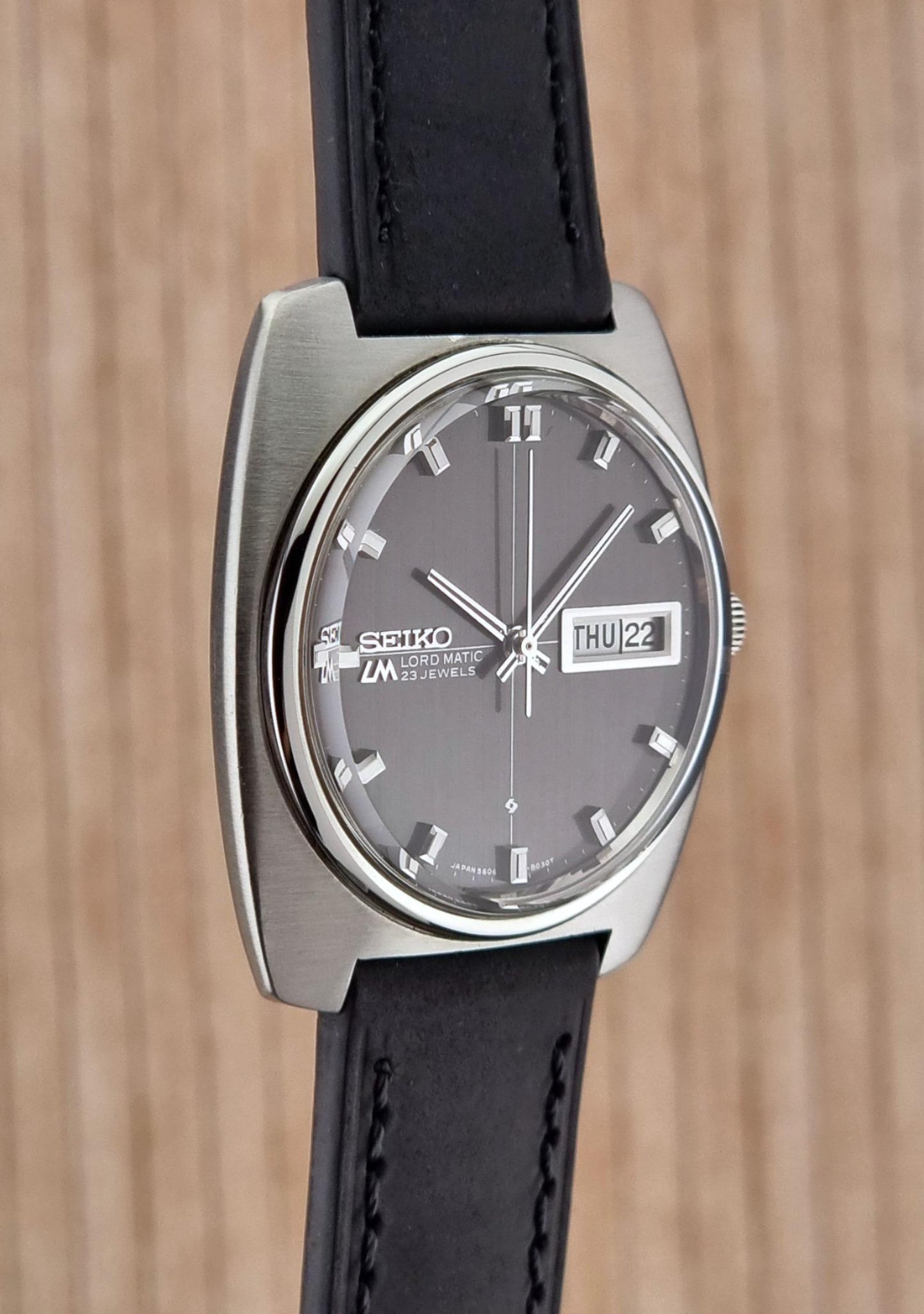 Side view of a Seiko Lord Matic watch with black strap on a wooden background